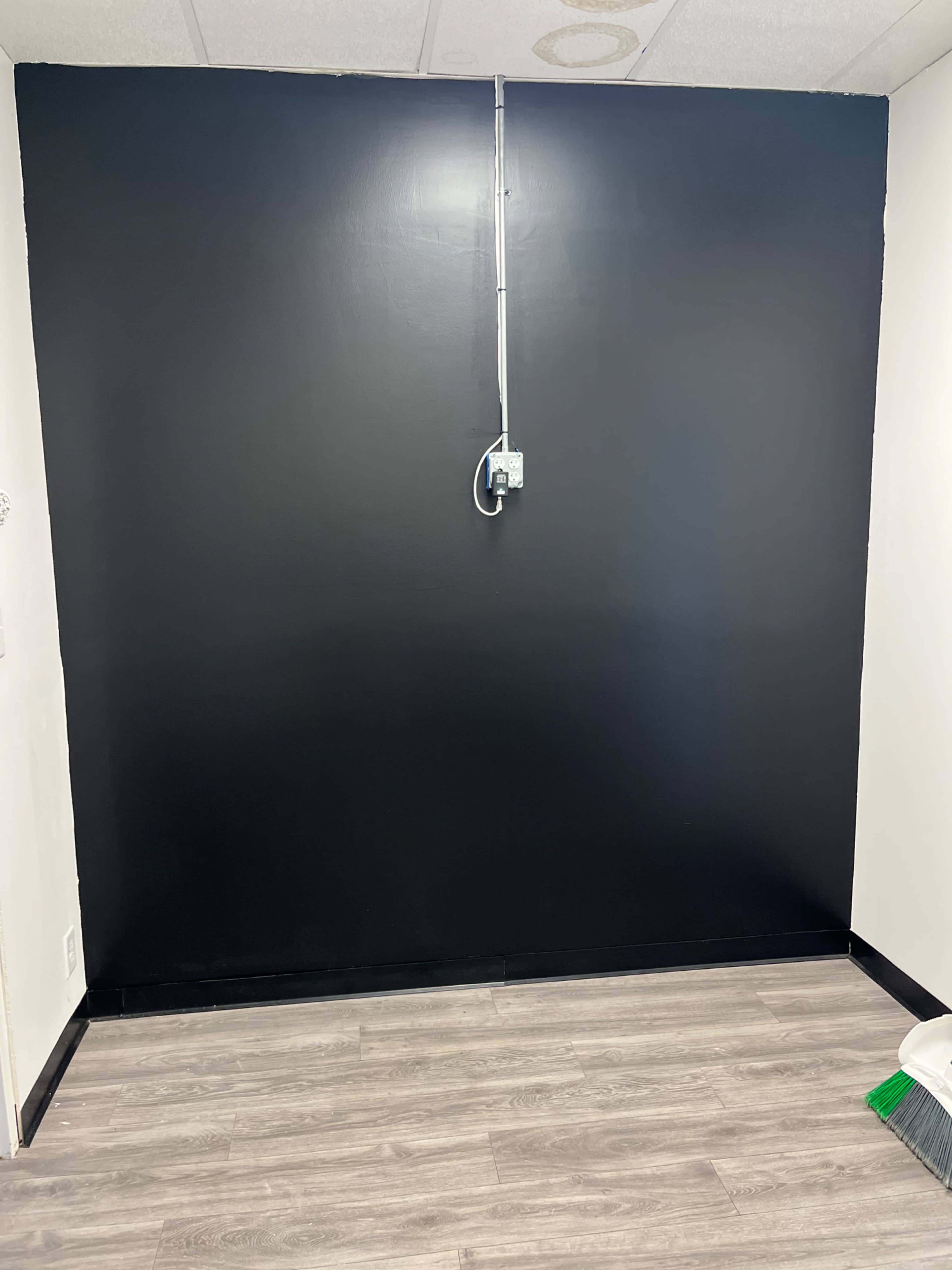 A bare room with a black-painted wall and a gray wooden floor, along with an electrical outlet mounted on the wall.