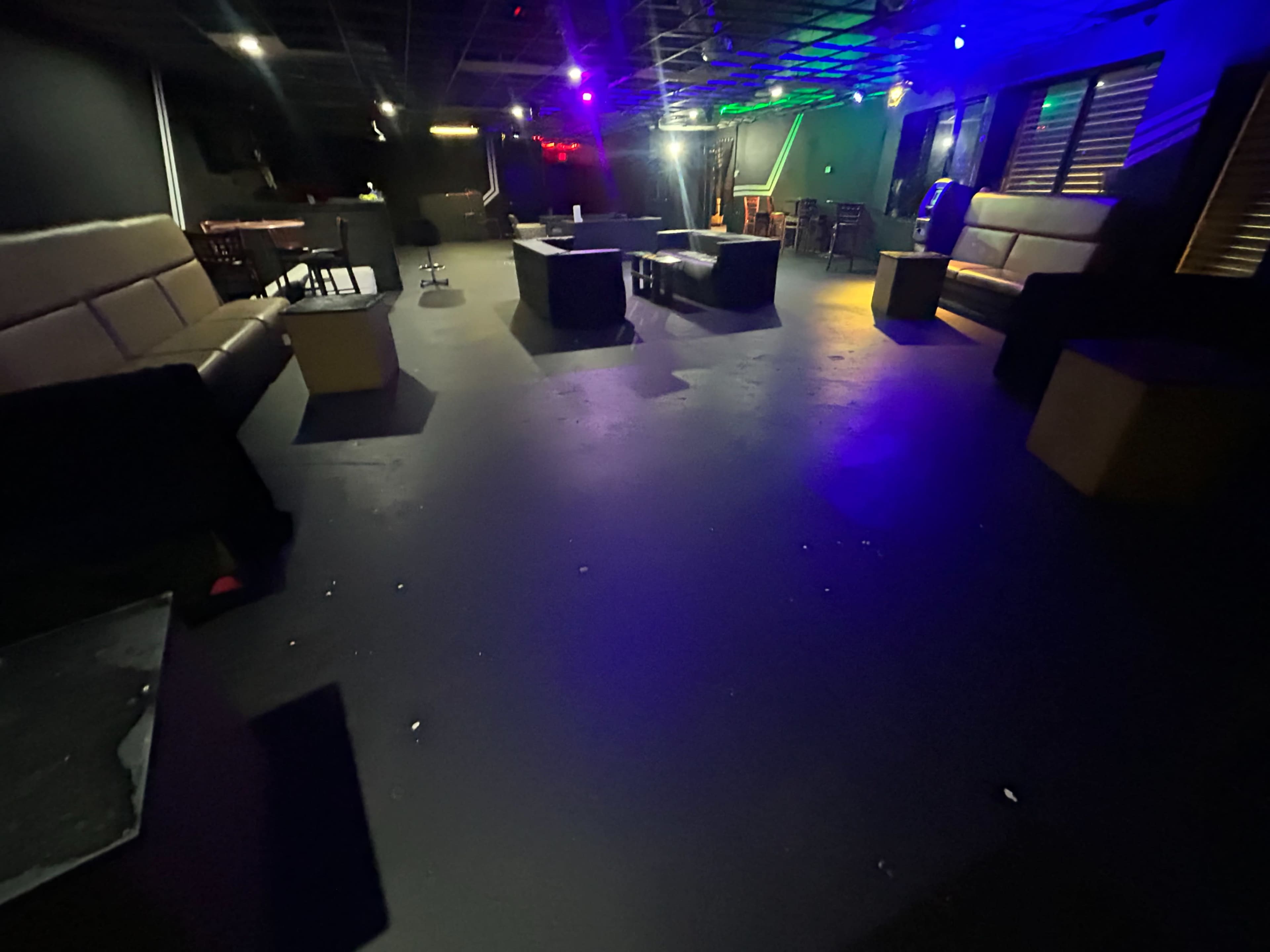 The image shows a dimly lit lounge area with seating, tables, and colorful ambient lights.