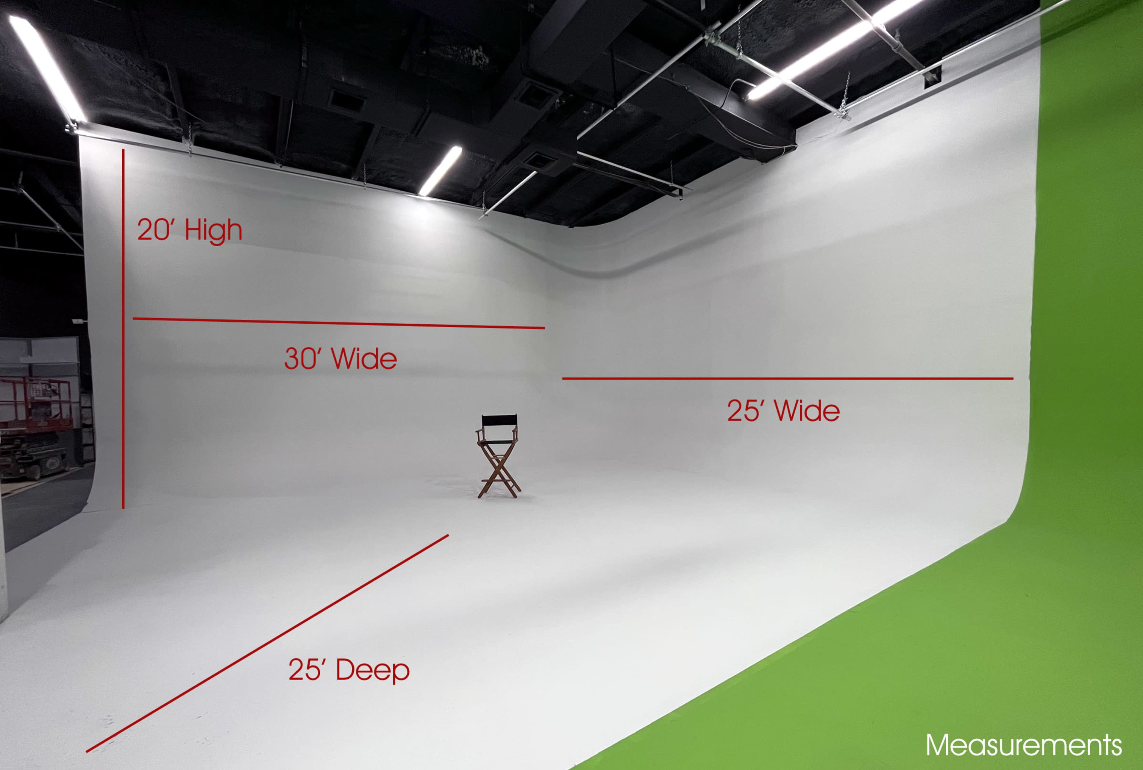 A professional studio space with a white cyc wall and a green screen, featuring a single director's chair in the center.