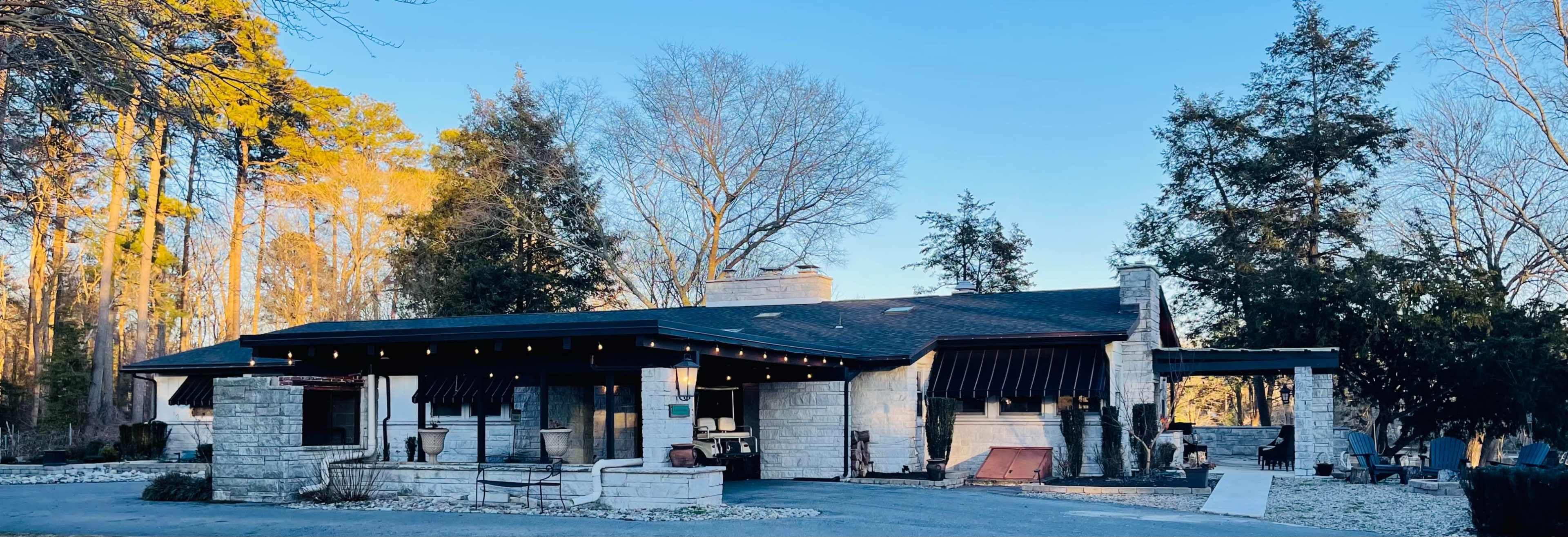 A stone building surrounded by trees, featuring a flat roof and large windows, with some outdoor furnishings visible.