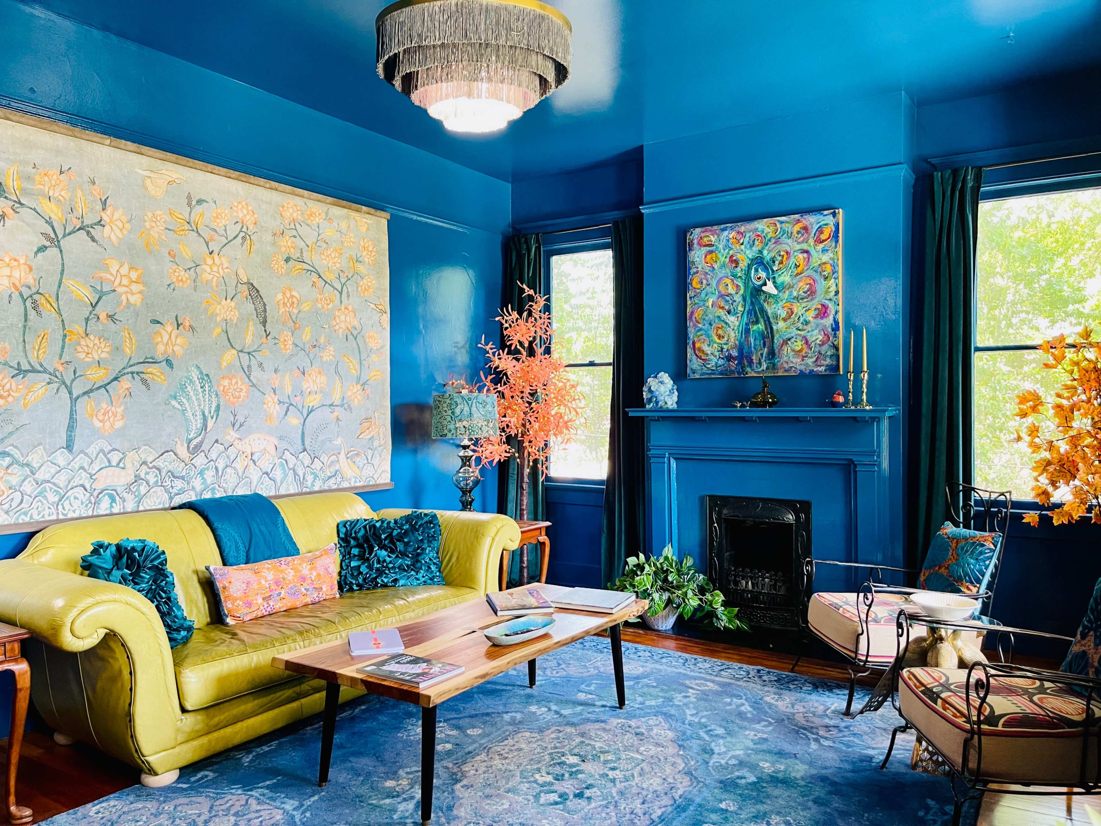 The room features a vibrant blue wall, a yellow couch, and decorative artwork complemented by plants and a fireplace.