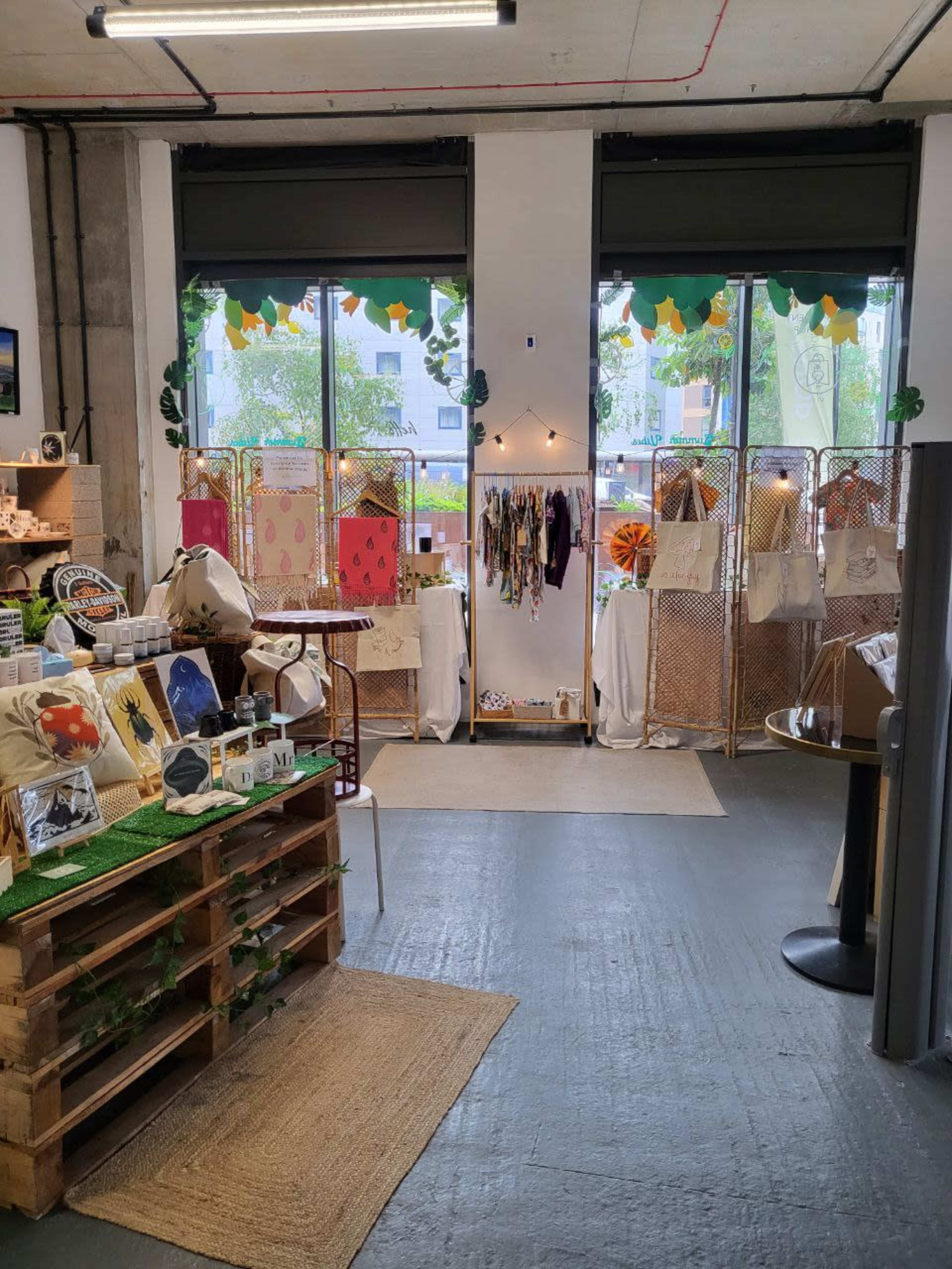 A boutique space featuring handmade crafts, displayed on wooden pallets and stands, with large windows letting in natural light.