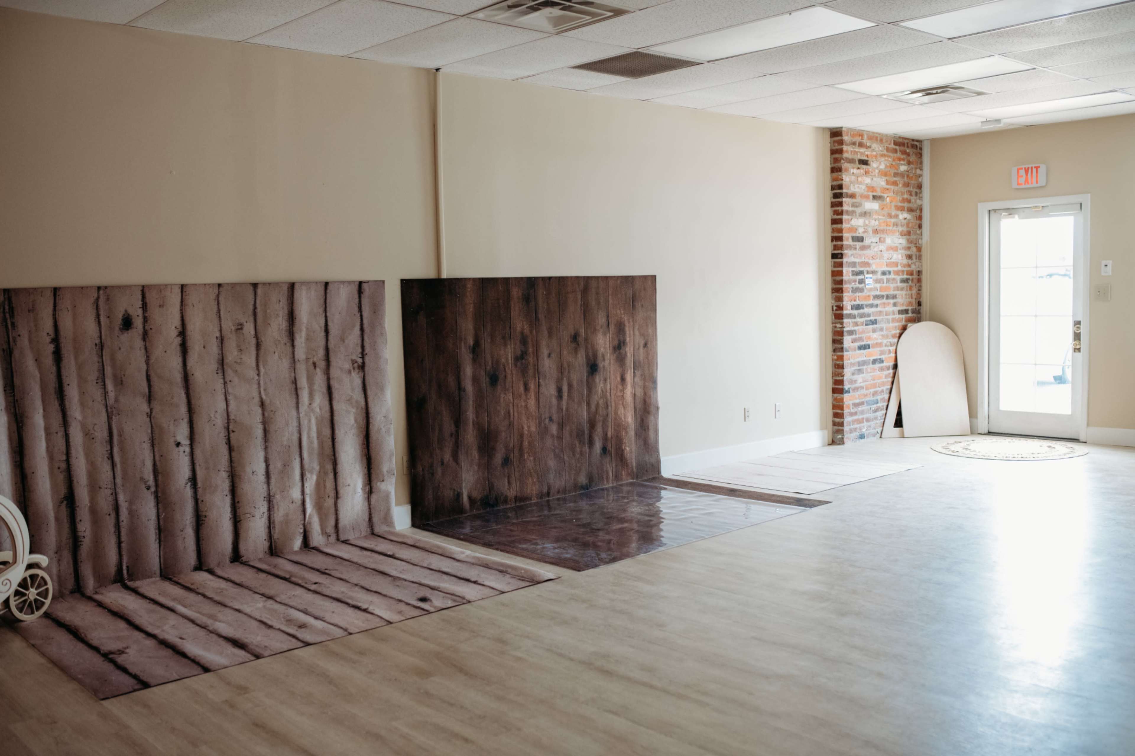 The image shows an empty indoor space with wooden texture backdrops on the floor and a light-colored wall with a door and window.