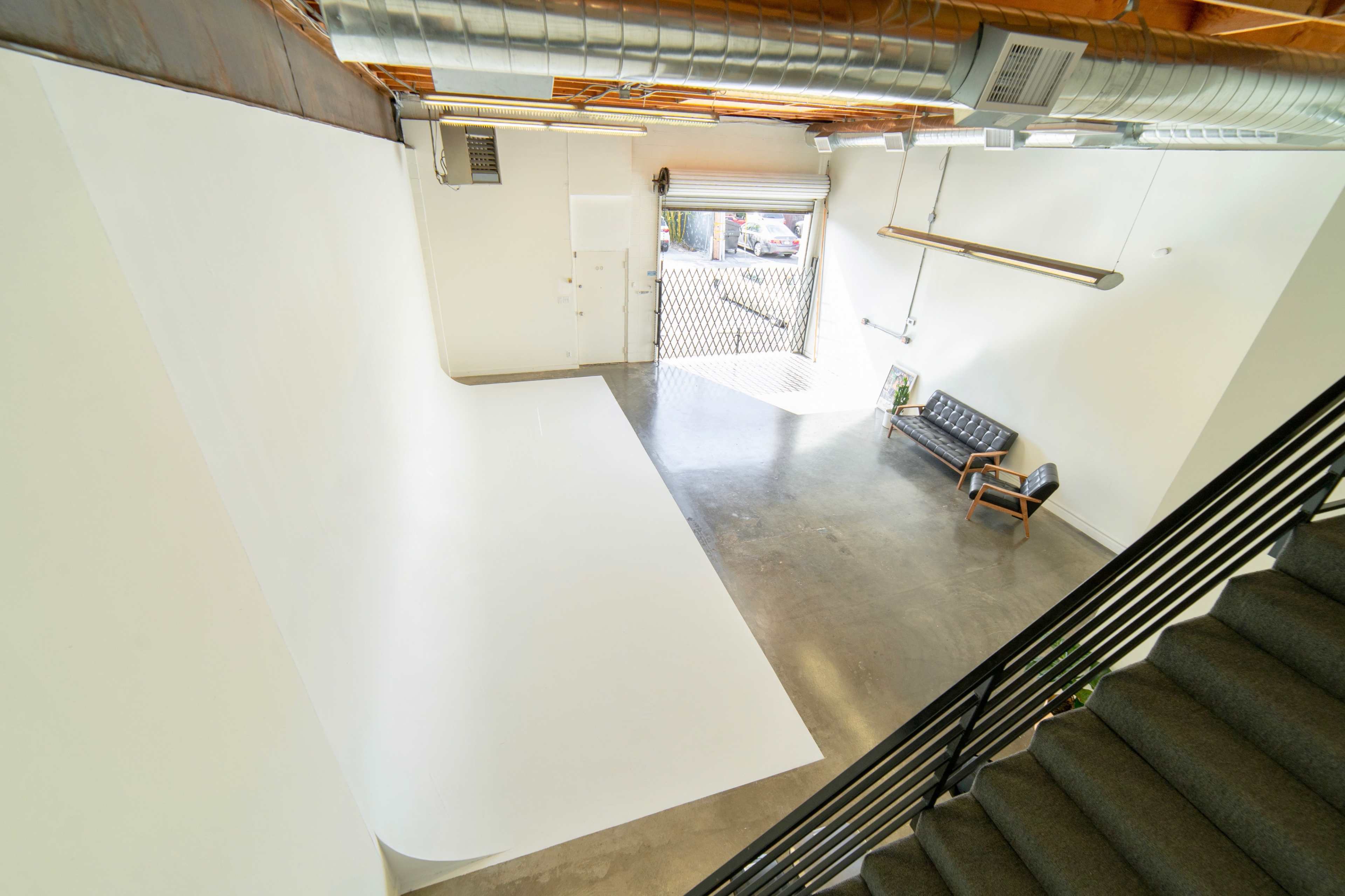 A spacious, minimalist studio with a large white backdrop, polished concrete floor, and a modern chair near a window.