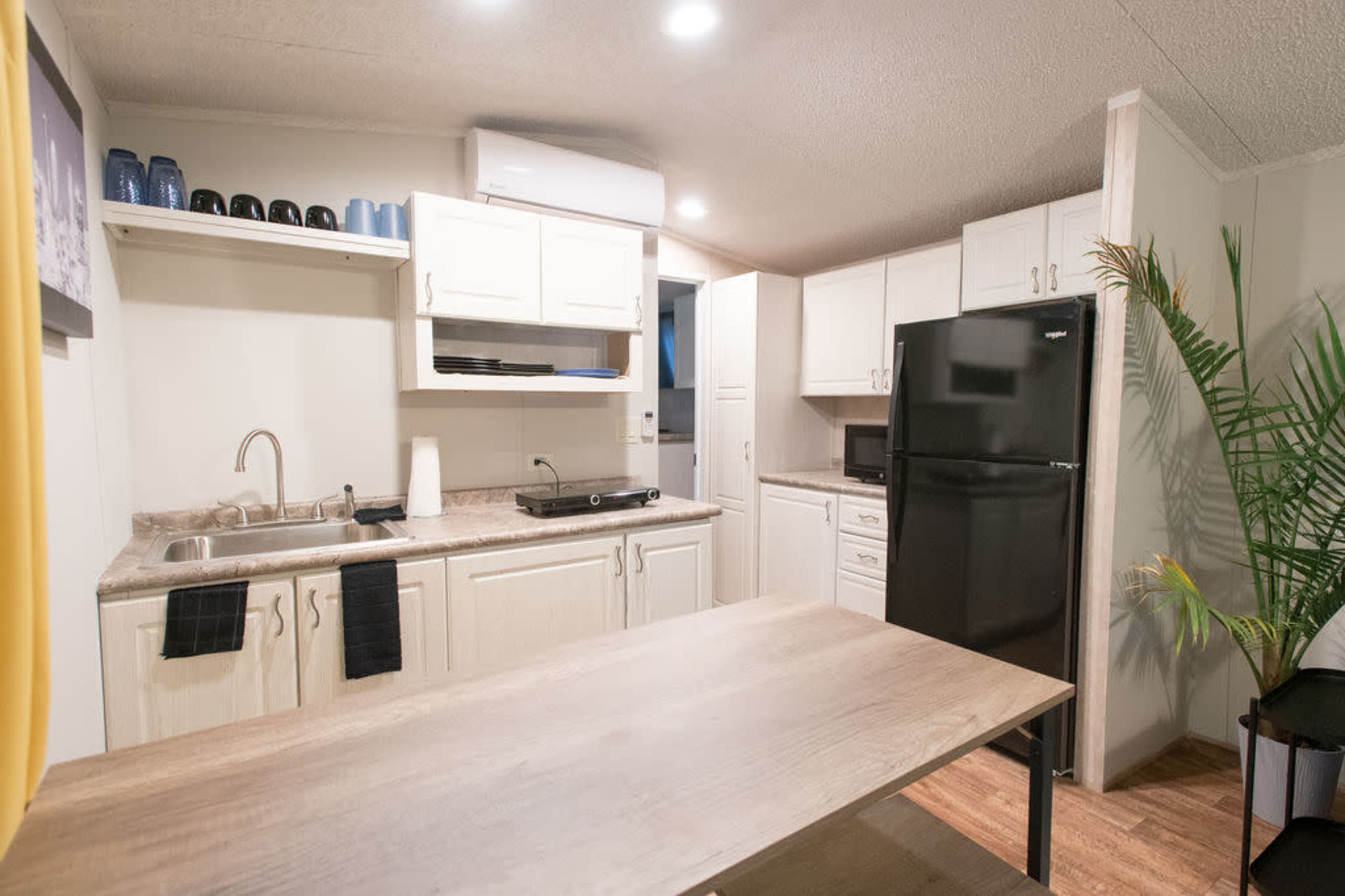 A modern kitchen with white cabinets, a black refrigerator, a small table, and a sink area.