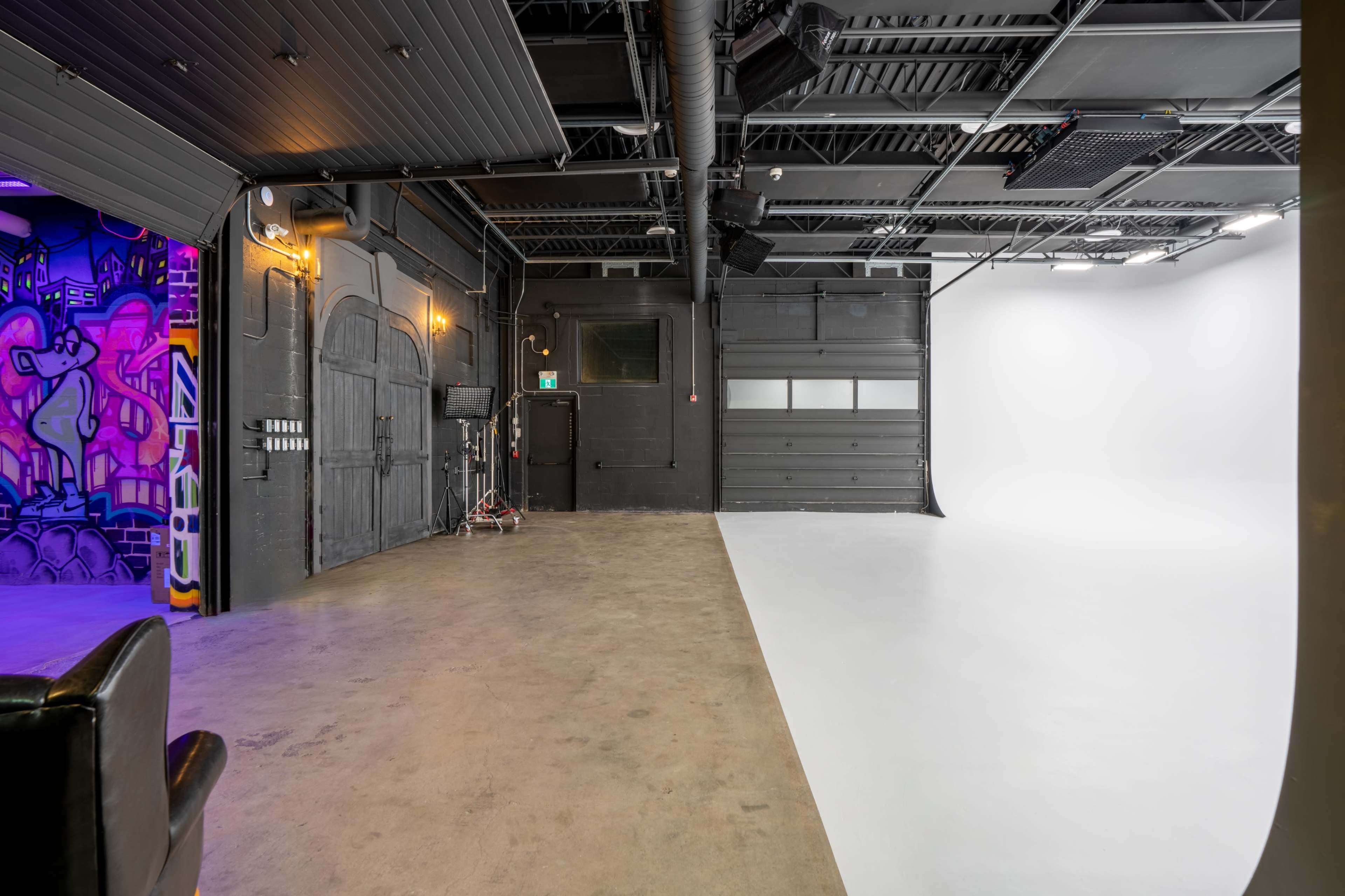 The image shows a spacious studio environment with a concrete floor, one side featuring a vibrant mural and the other side a plain white backdrop.