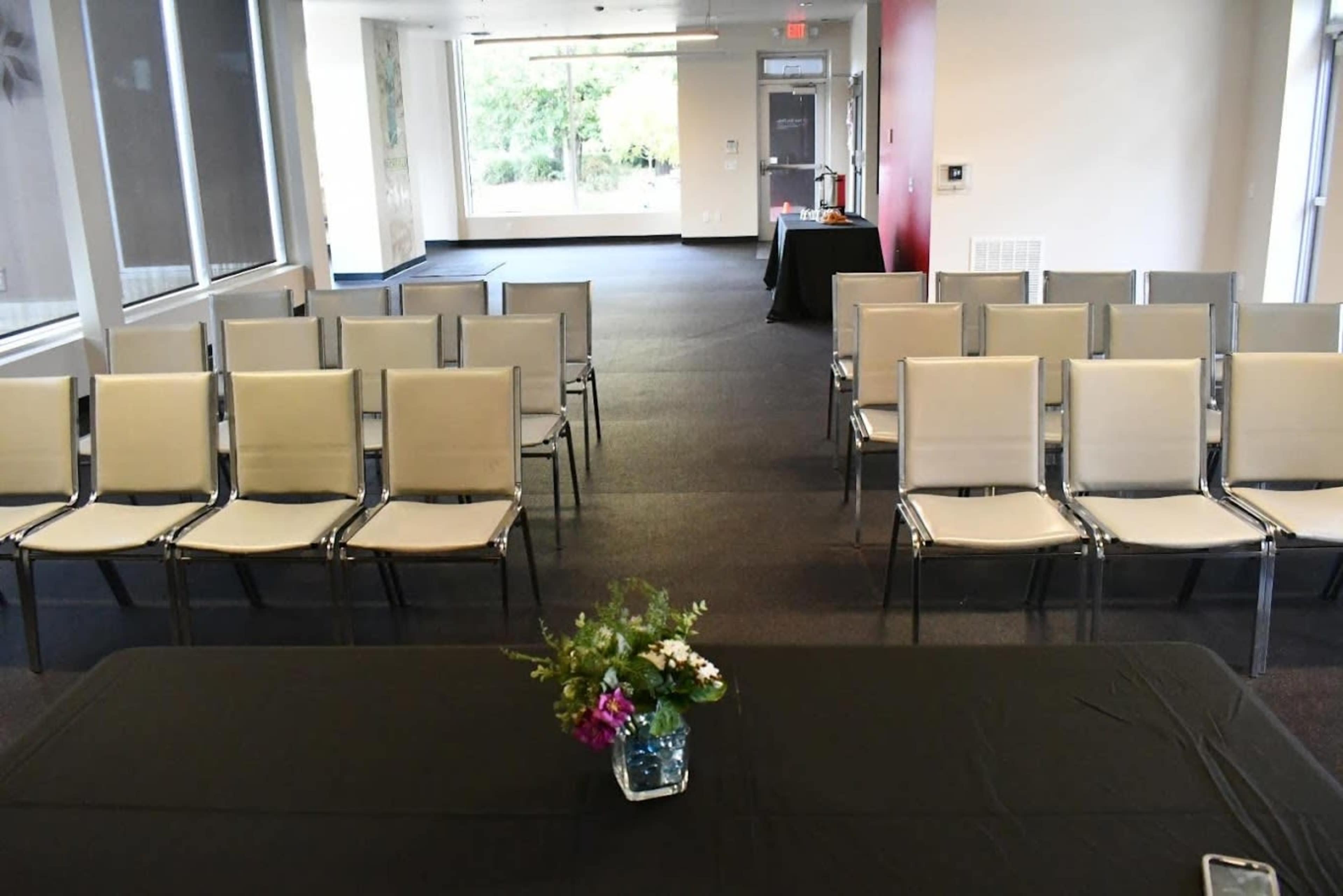 A spacious room set up with rows of beige chairs facing a table adorned with flowers at the front.