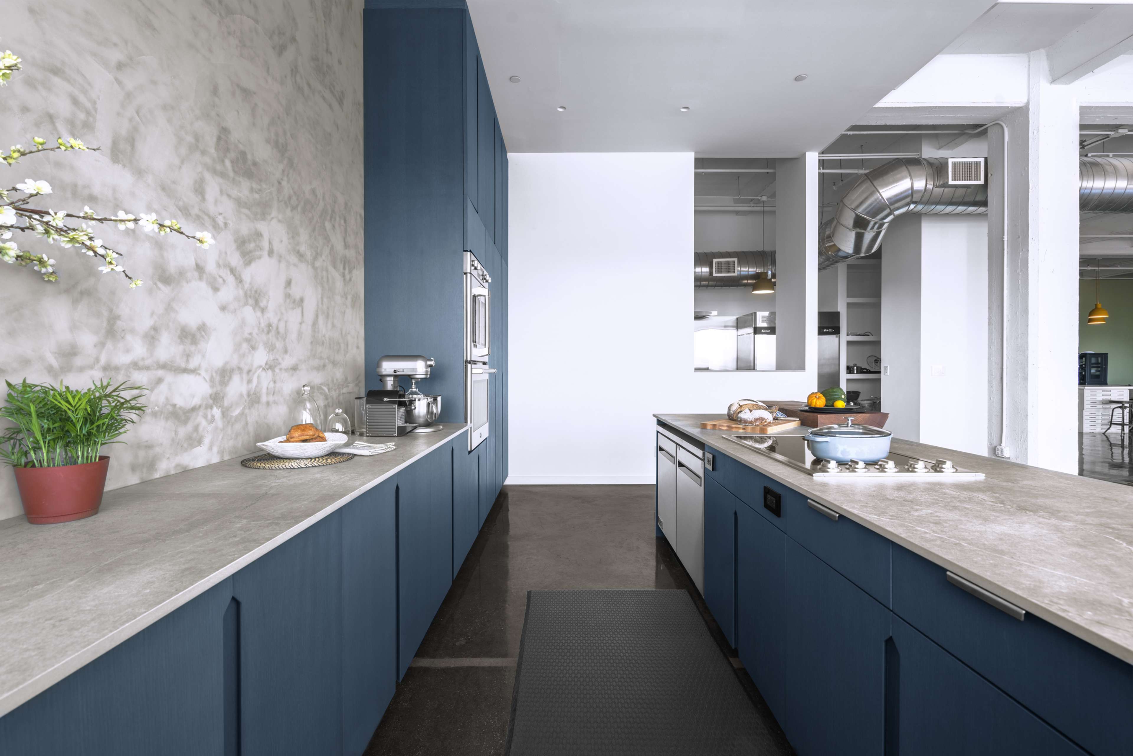 A modern kitchen features blue cabinetry, a concrete countertop, and stainless steel appliances, with a minimalist design and industrial elements.