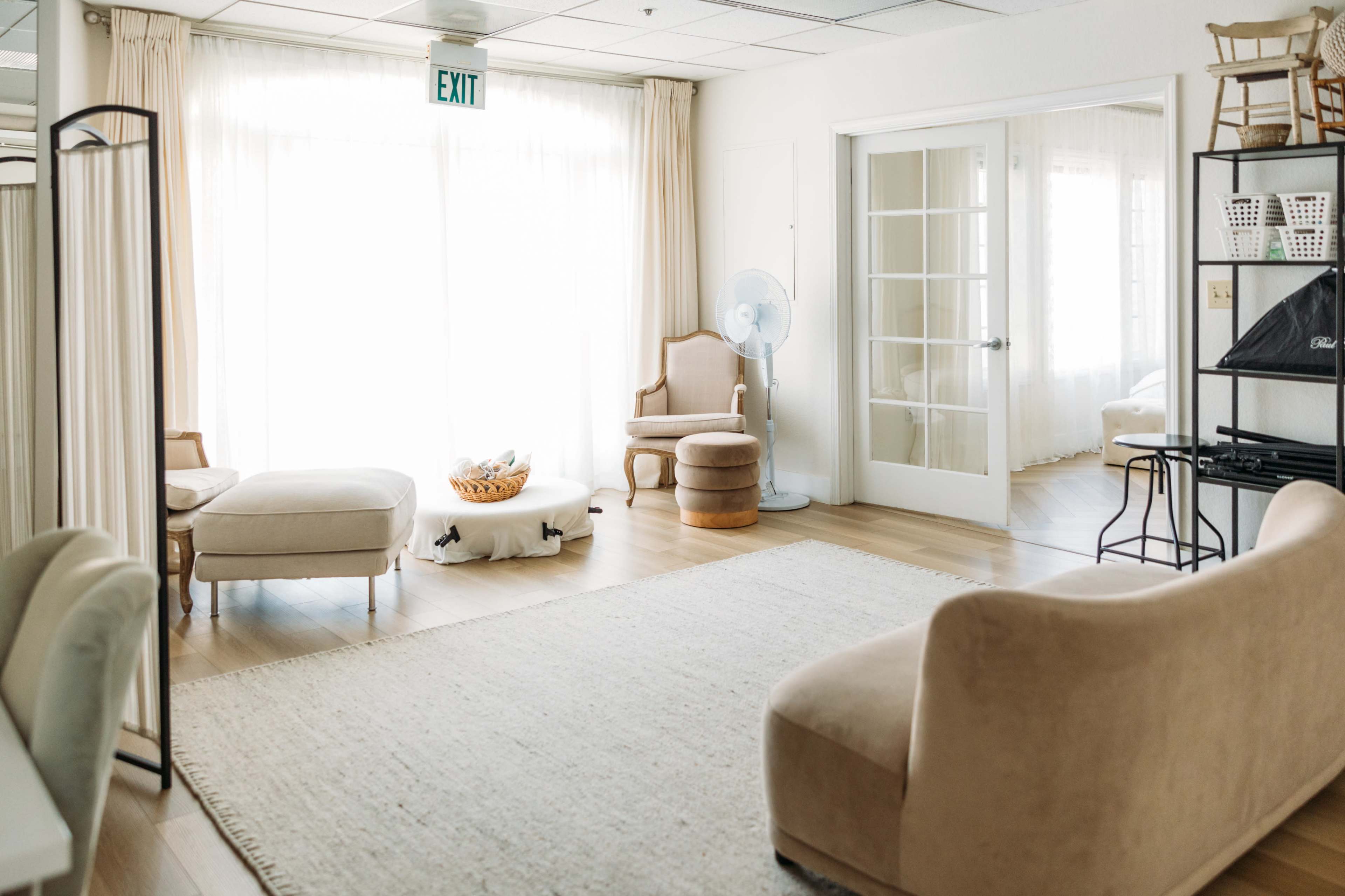 A bright room with large windows, featuring a light-colored rug, a sofa, a chair, and a small table.