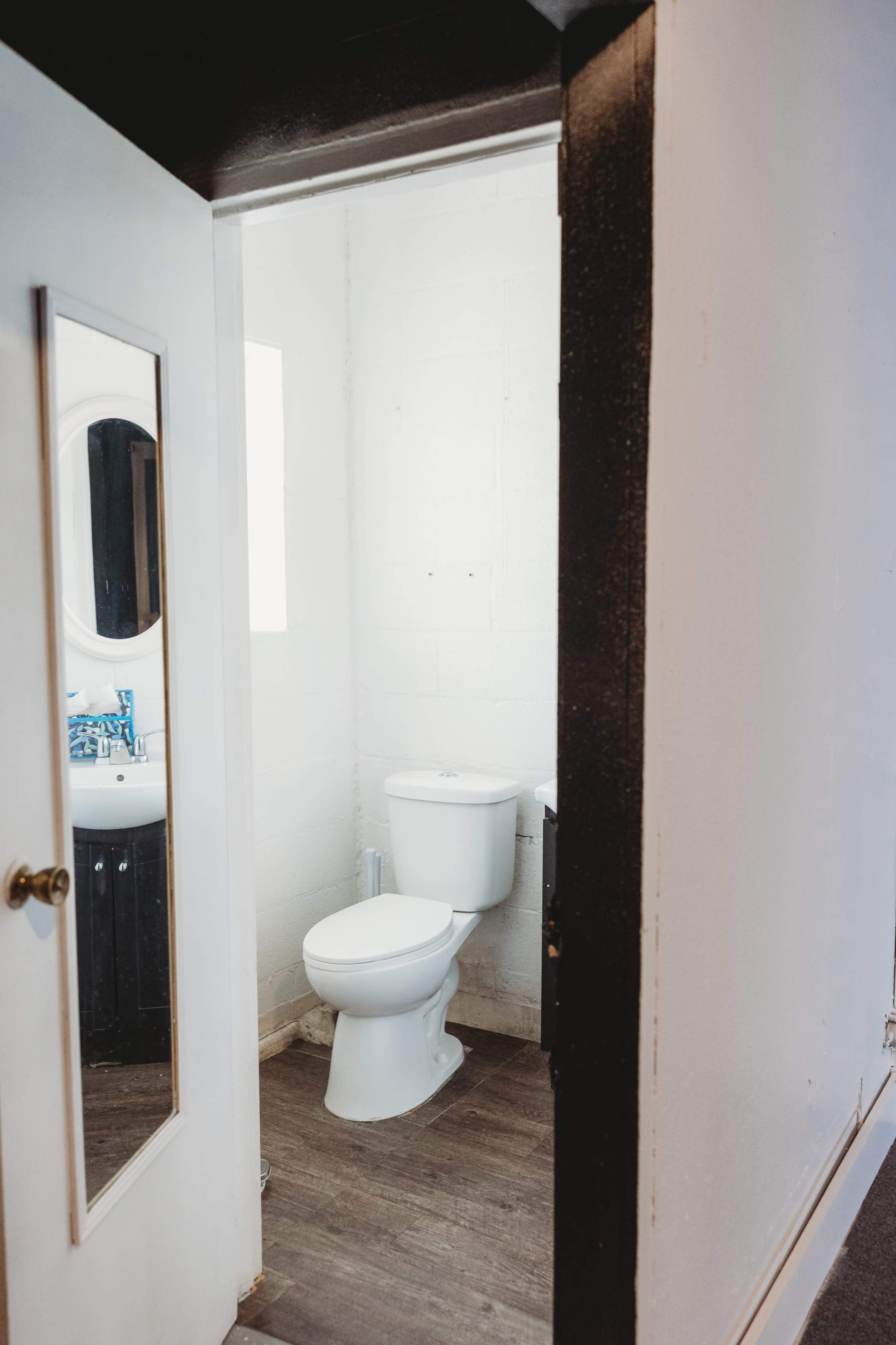 A bathroom with a toilet visible through a doorway, along with a mirror and a sink area in the background.