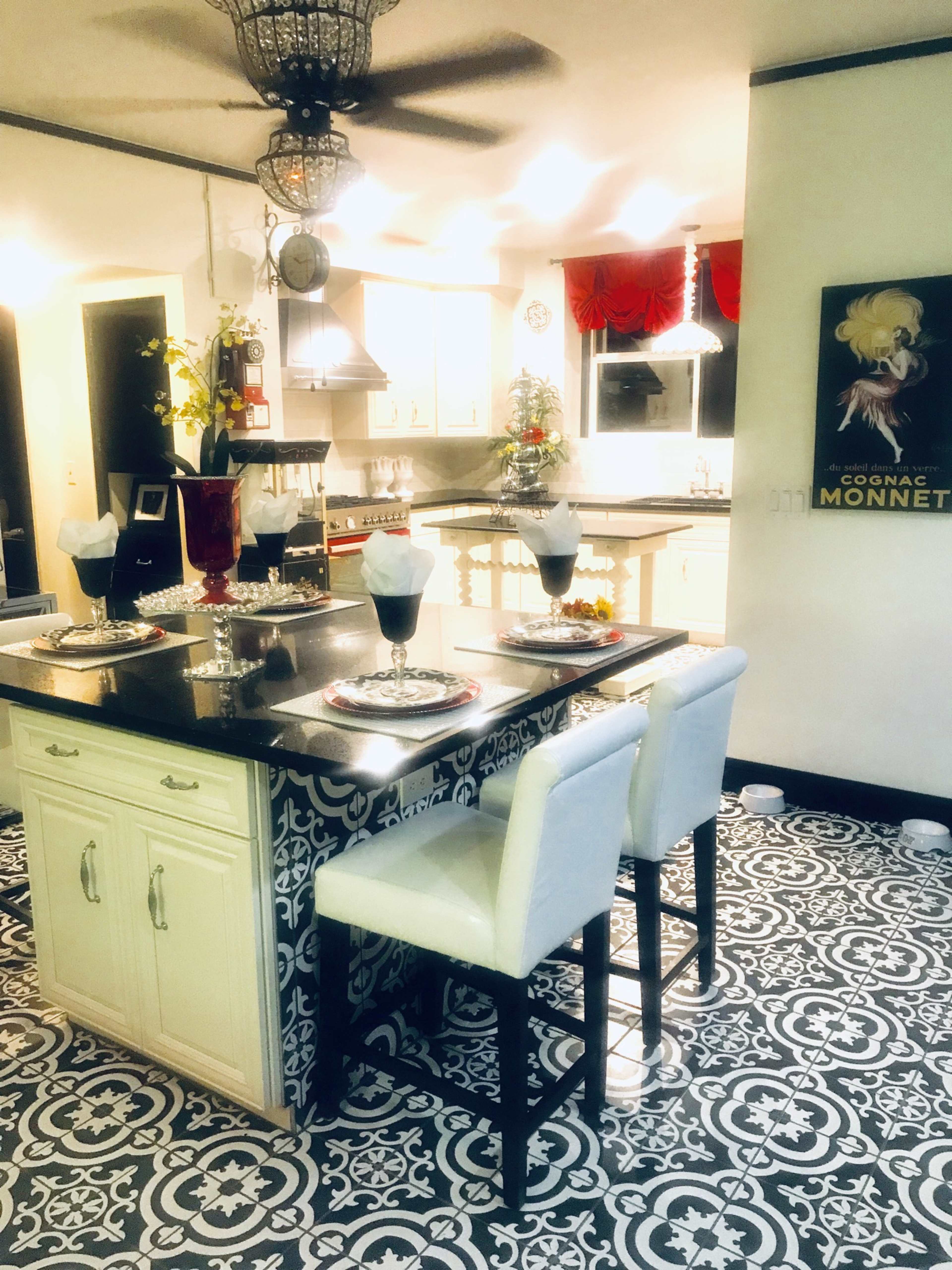 A modern kitchen with a decorative black and white tile floor, an island with seating, and various furnishings and decorations.