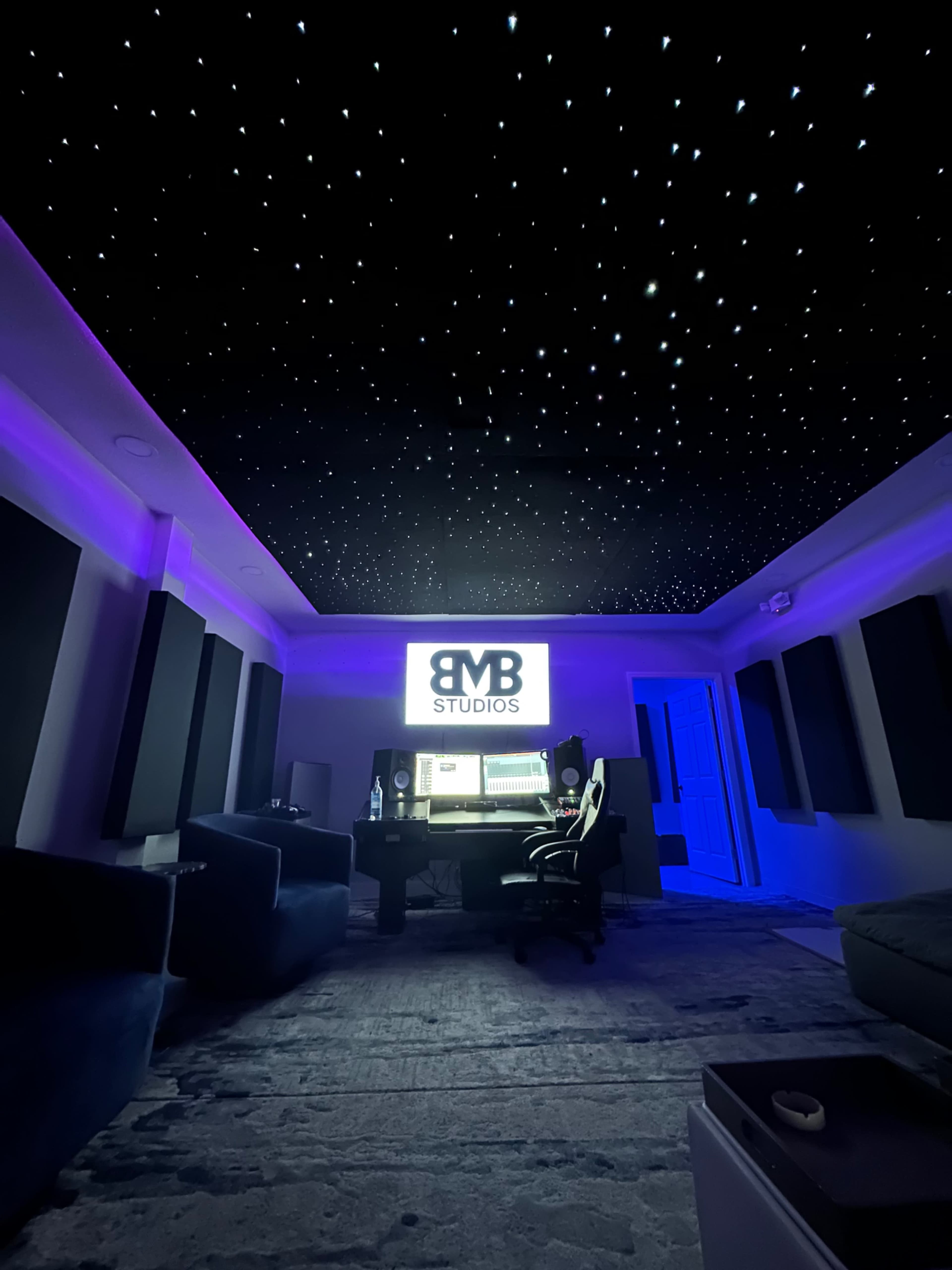 A music studio with a starry ceiling, purple lighting, and a workstation featuring monitors and sound equipment.