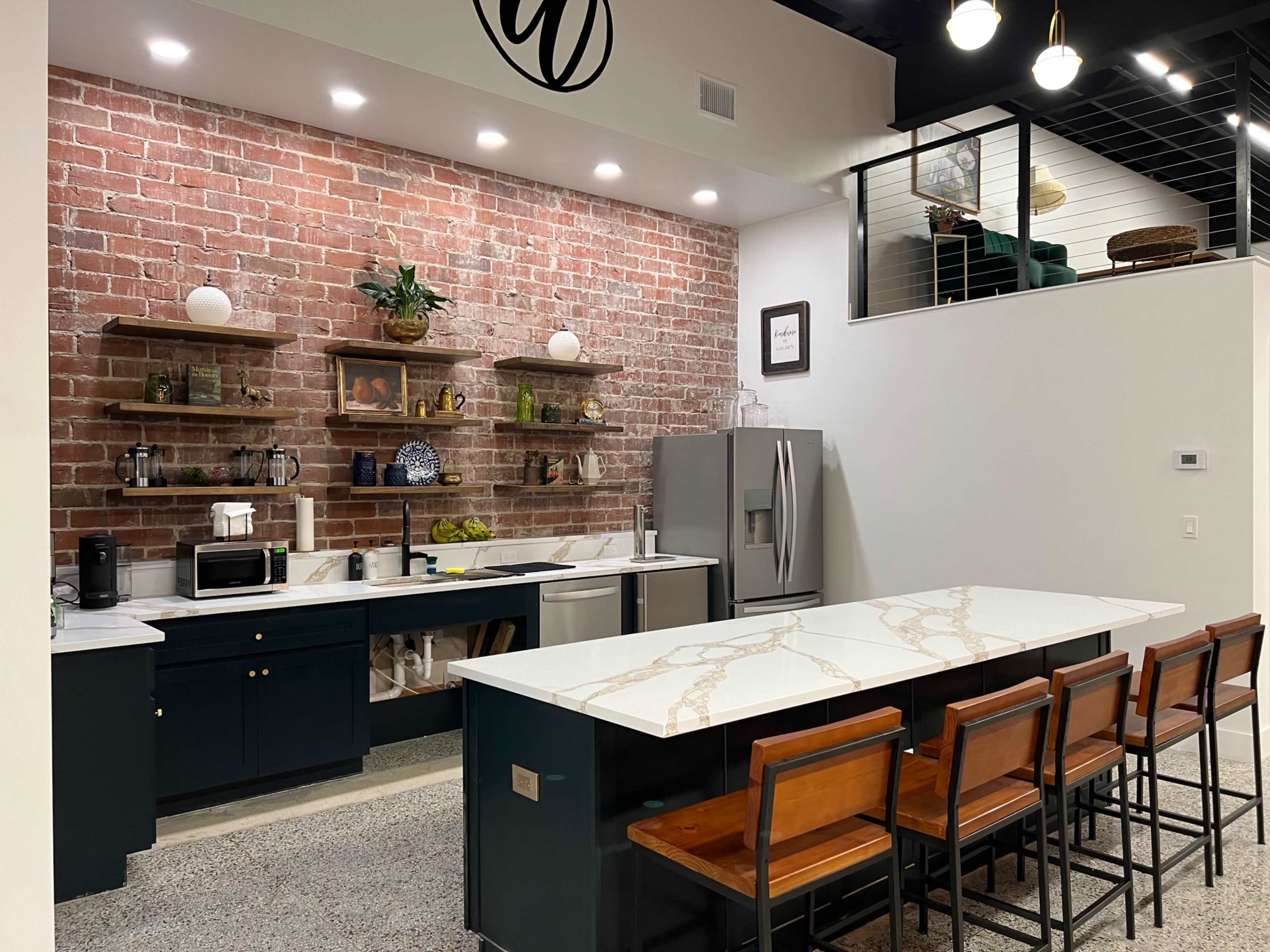 A modern kitchen with a brick wall, dark cabinetry, and a large island with a marble countertop and bar stools.
