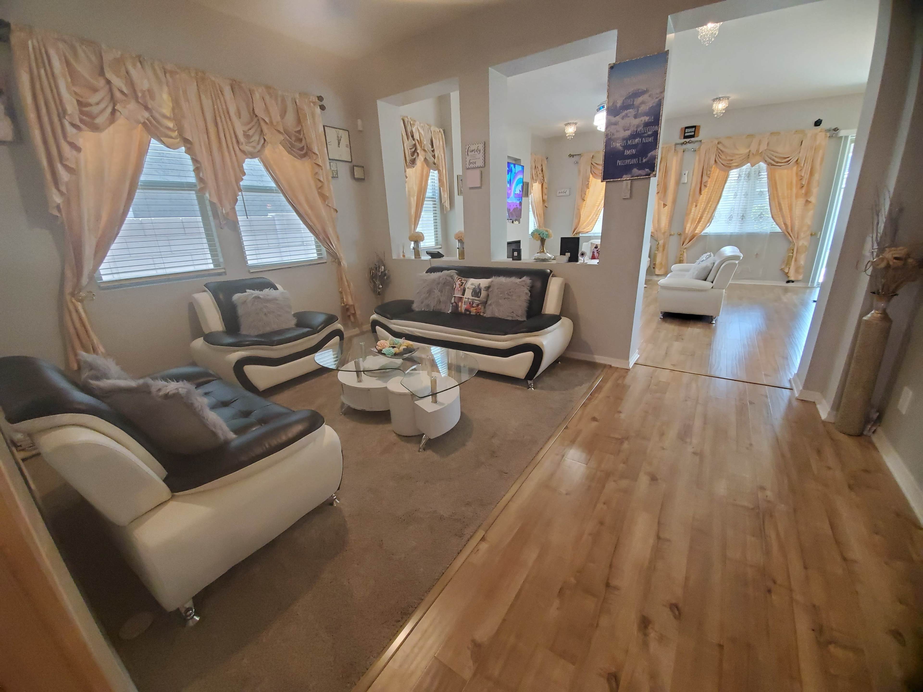 A modern living room with a beige rug, white and black sofas, decorative curtains, and a glass coffee table.