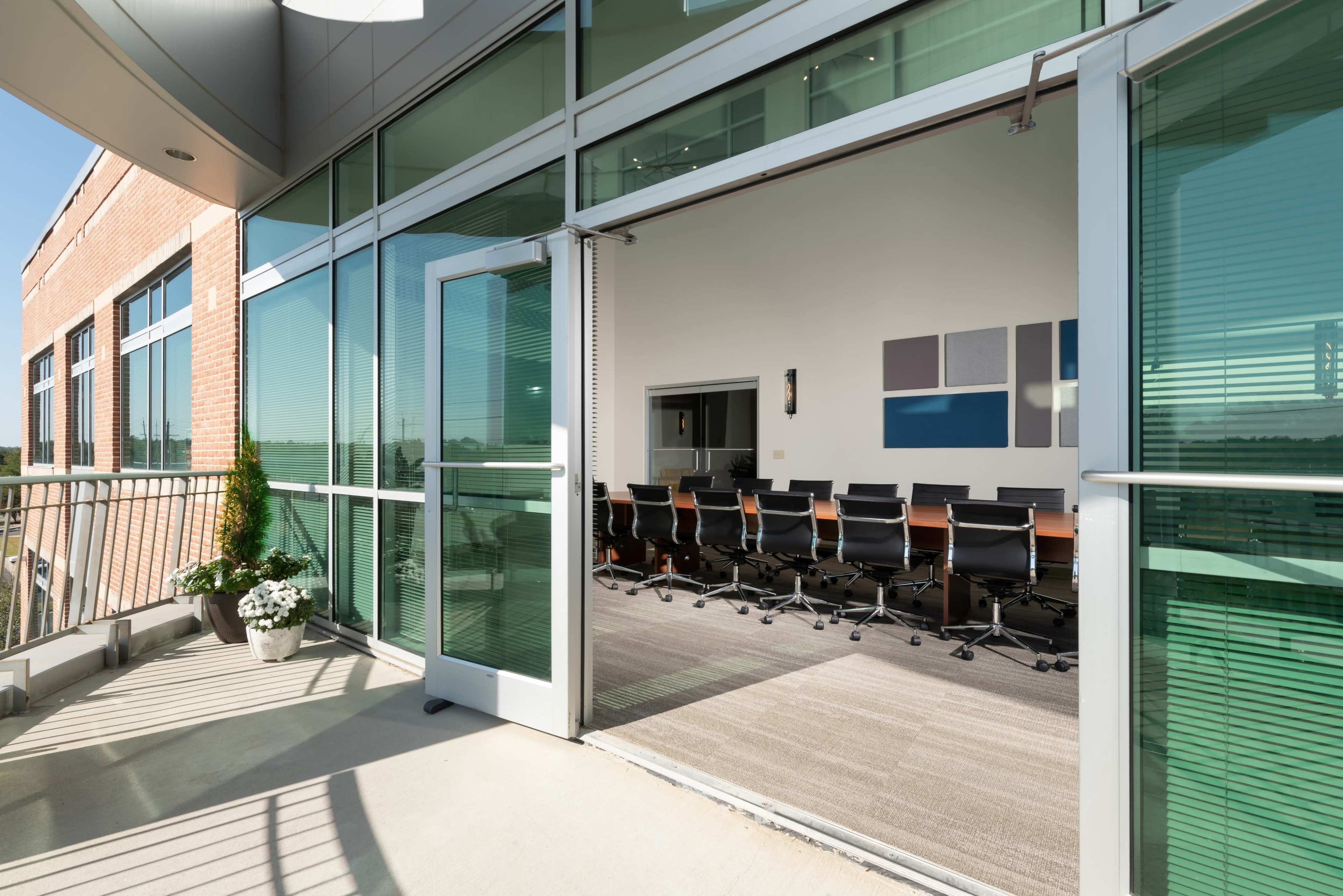 A spacious conference room with a long table and chairs is visible through large glass doors that open to a balcony.