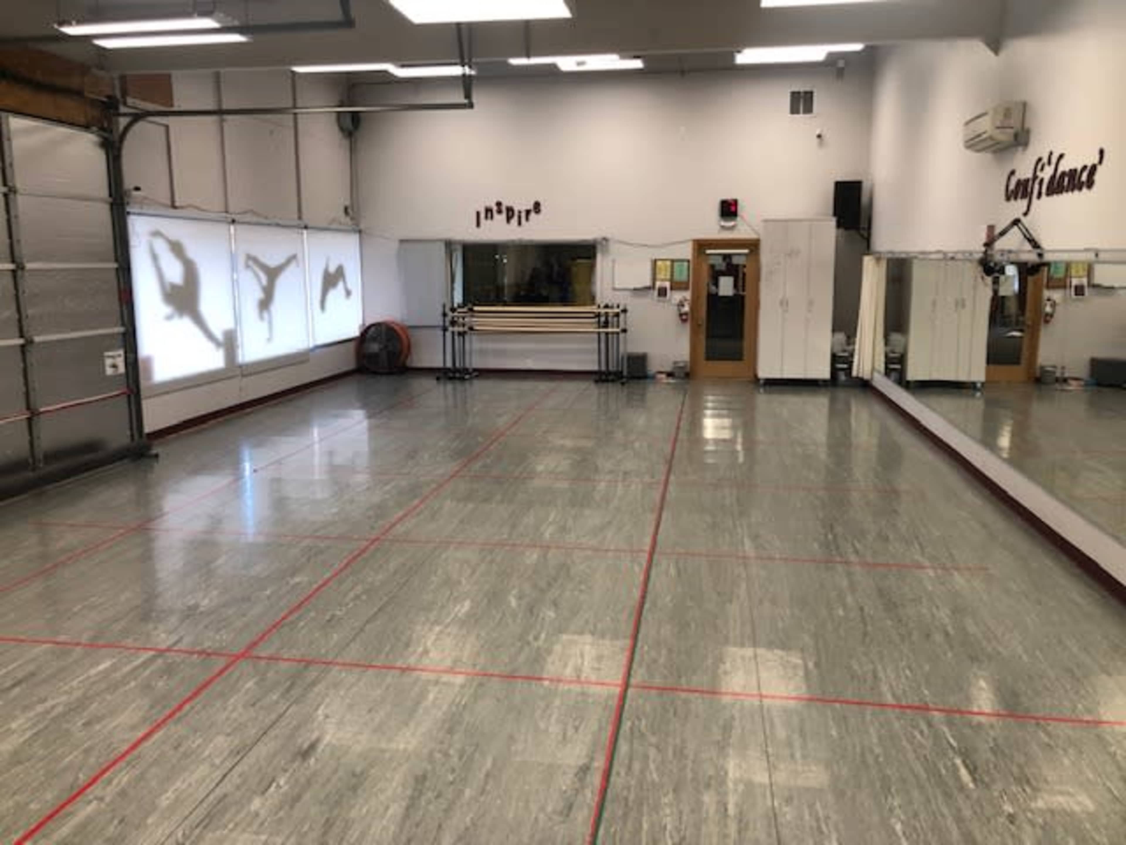 A dance studio with mirrored walls, a smooth floor, and silhouettes of dancers projected on one wall.