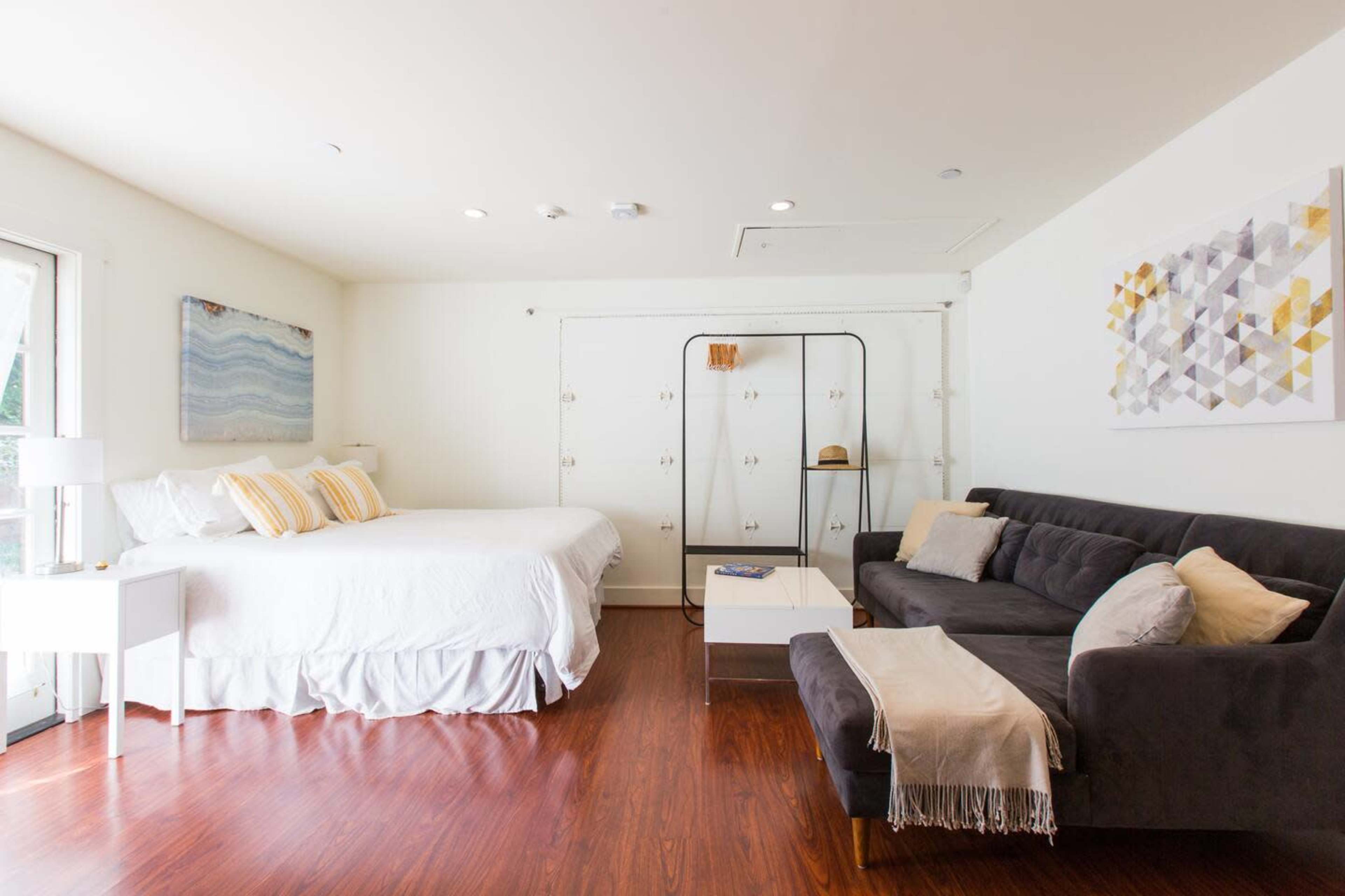 A well-lit bedroom featuring a bed, a dark sofa, a coffee table, and a wardrobe against a white wall.