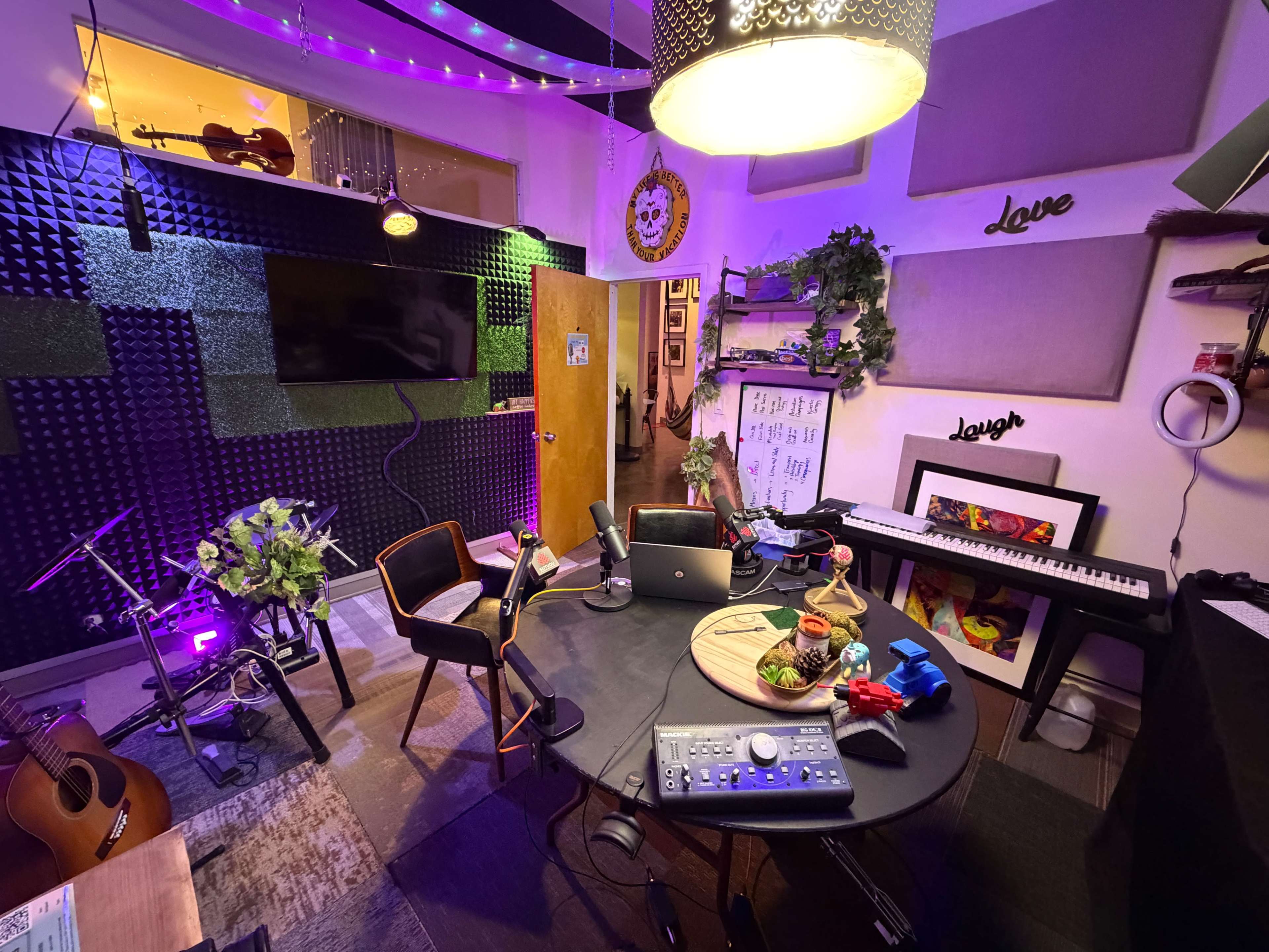 The image shows a creative workspace with musical instruments, a round table, chairs, and colorful lighting.