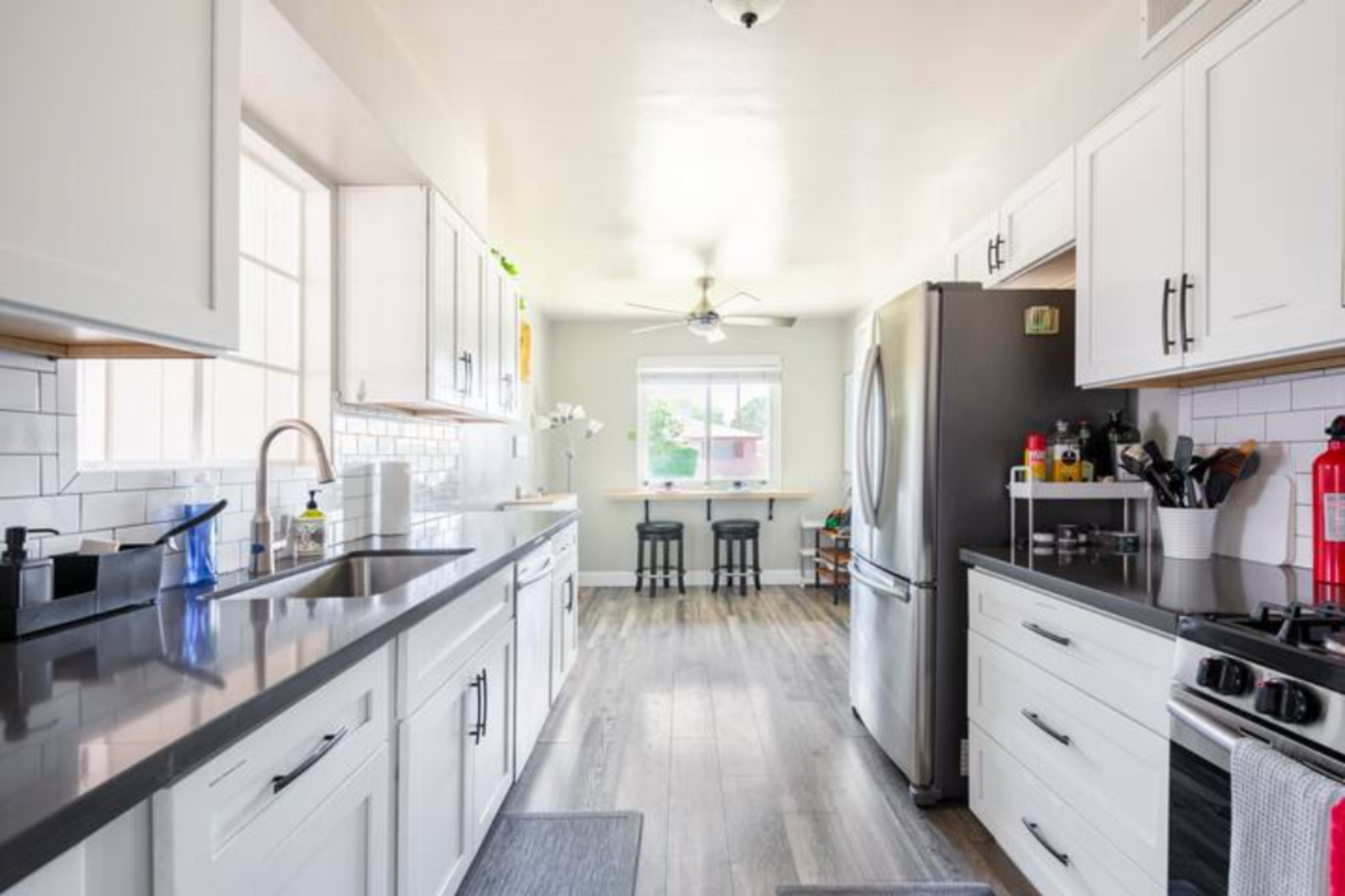 A modern kitchen featuring white cabinetry, stainless steel appliances, and a breakfast bar with two stools.