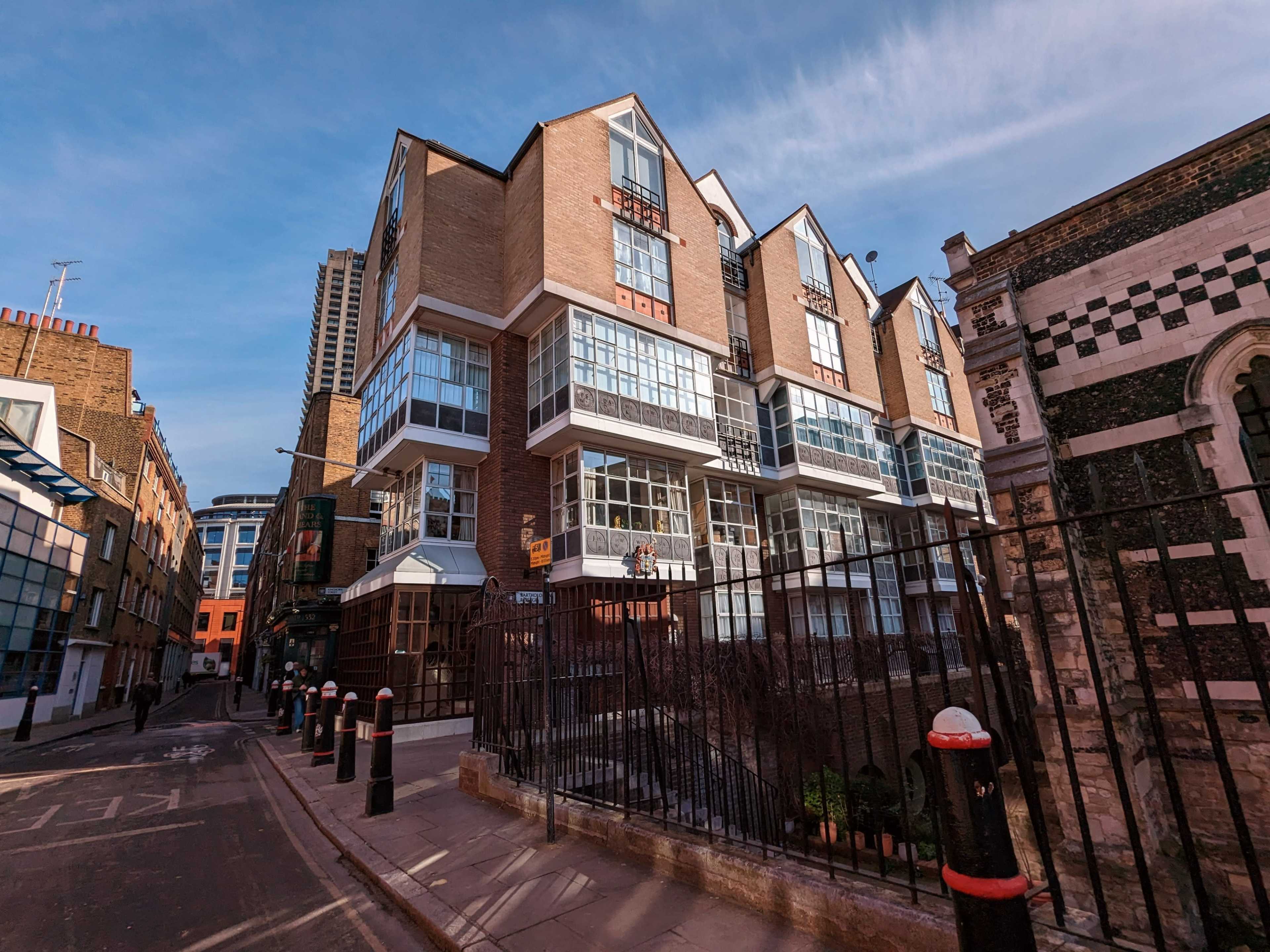 A modern building with large glass windows and a distinctive architectural design, situated at the end of a narrow street lined with barriers.