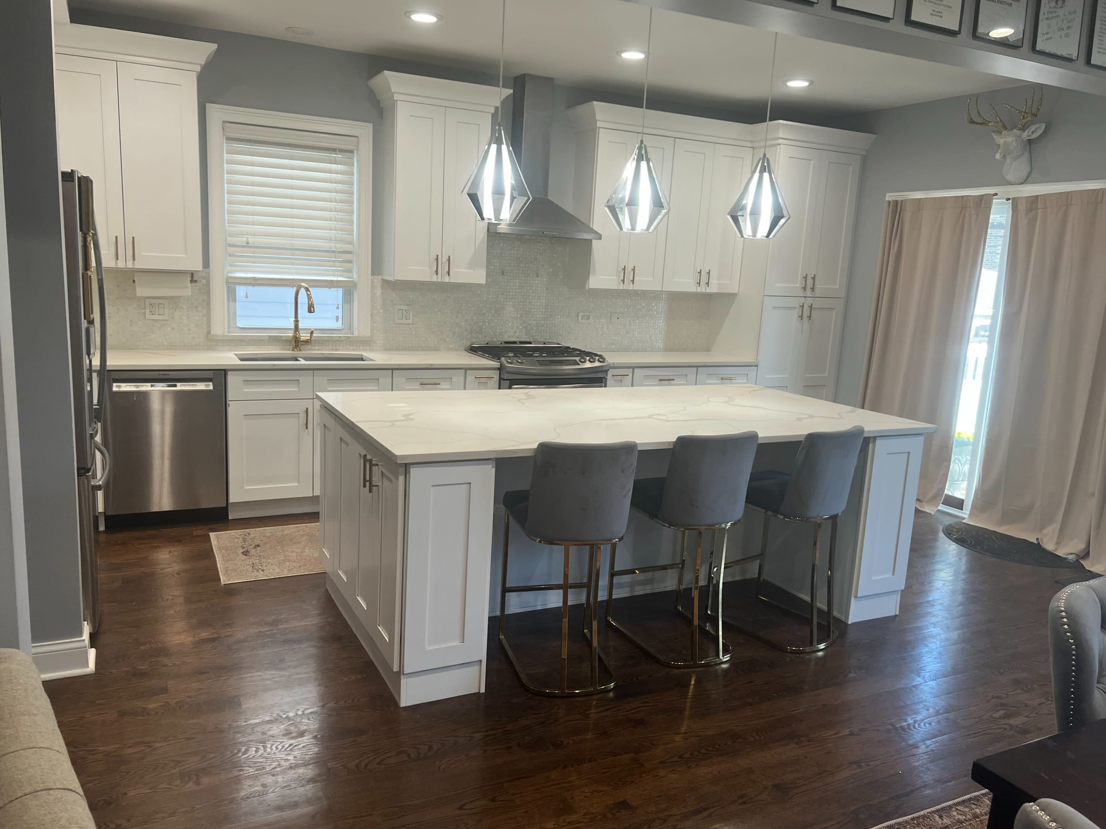 The image shows a modern kitchen featuring white cabinetry, a large island with bar seating, stainless steel appliances, and pendant lighting.