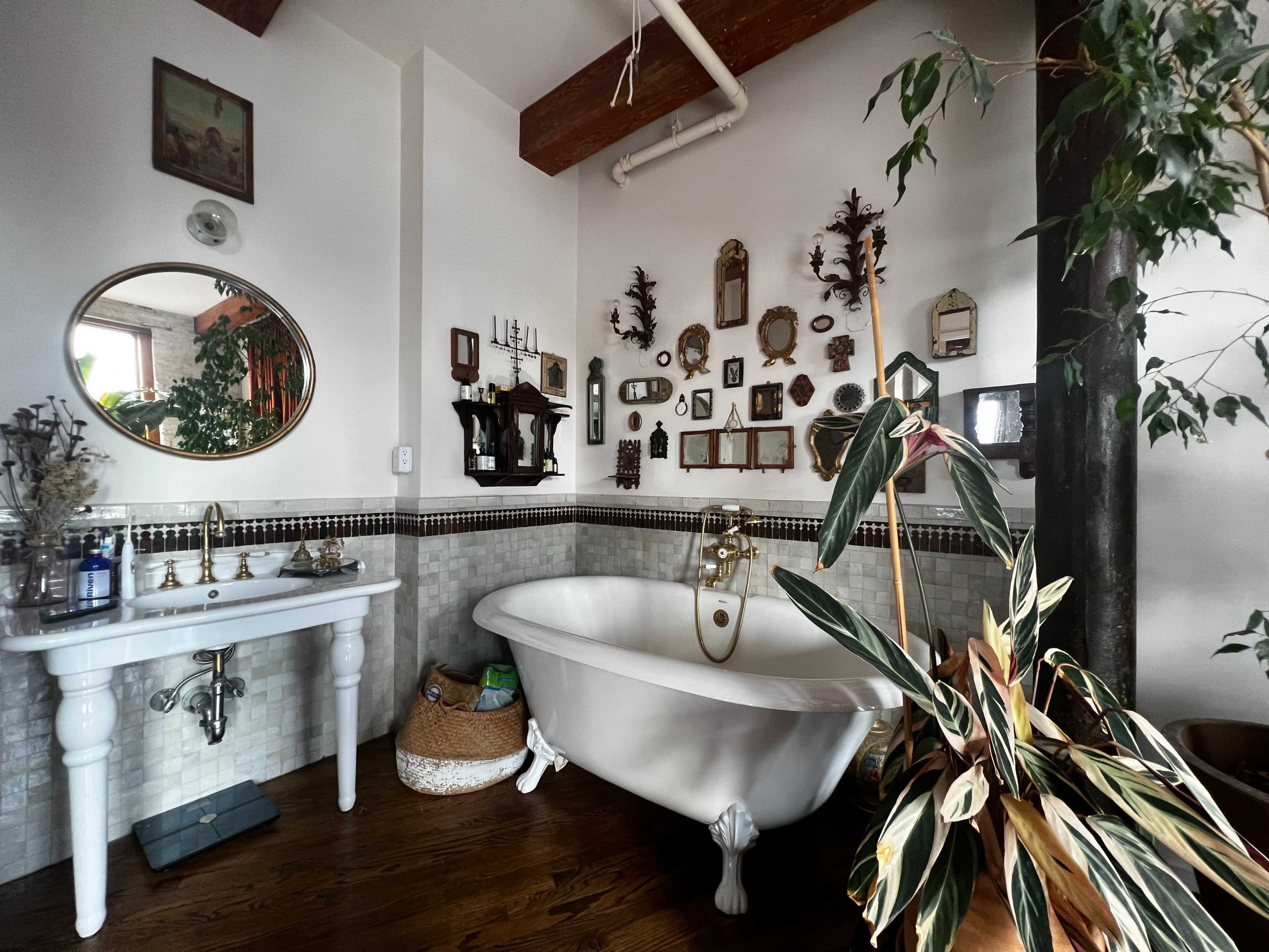 The bathroom features a freestanding clawfoot bathtub, a vintage-style sink, and a wall adorned with various framed art and decorative items.