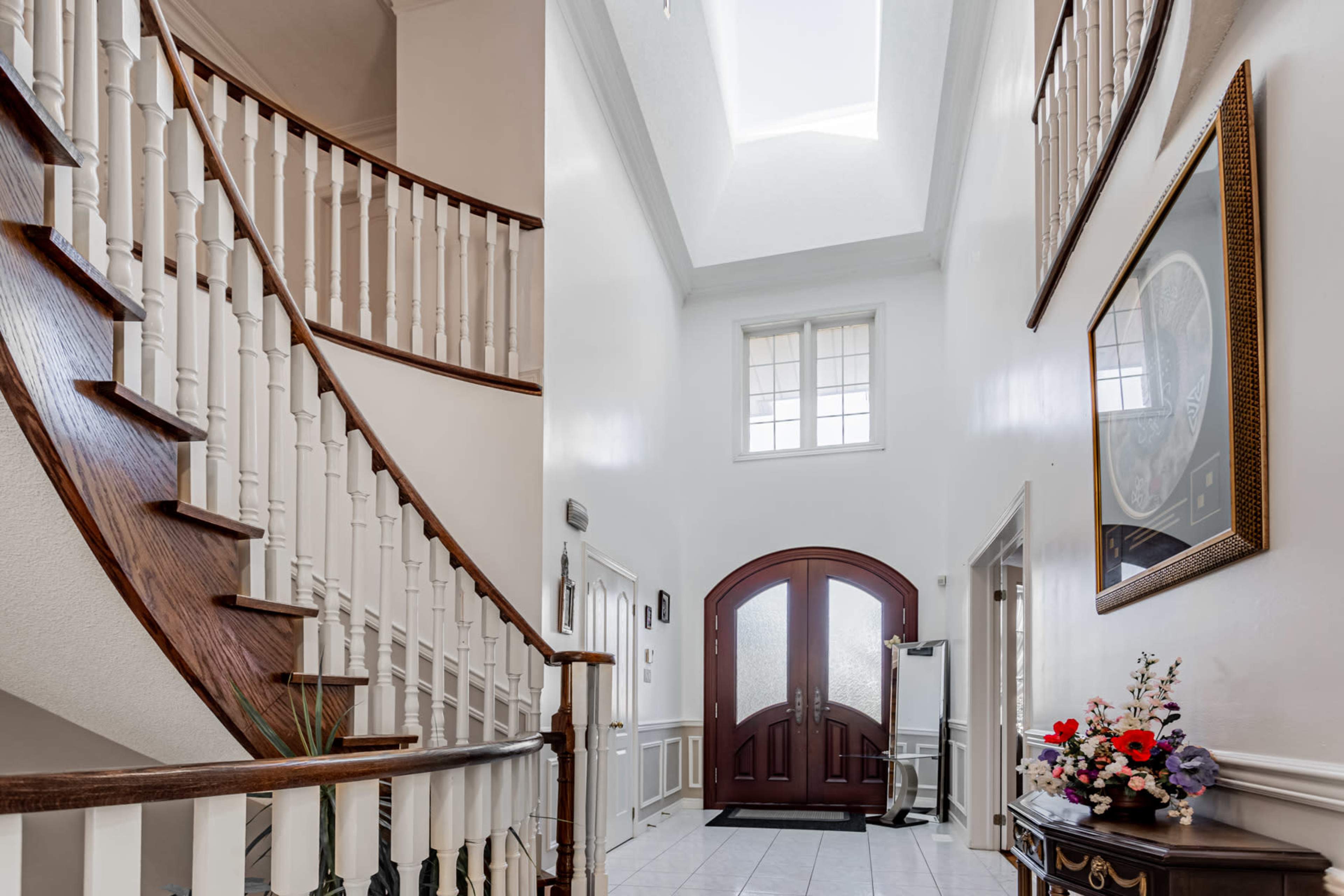 A spacious foyer with a spiral staircase, large double doors, and a decorative table with a floral arrangement.