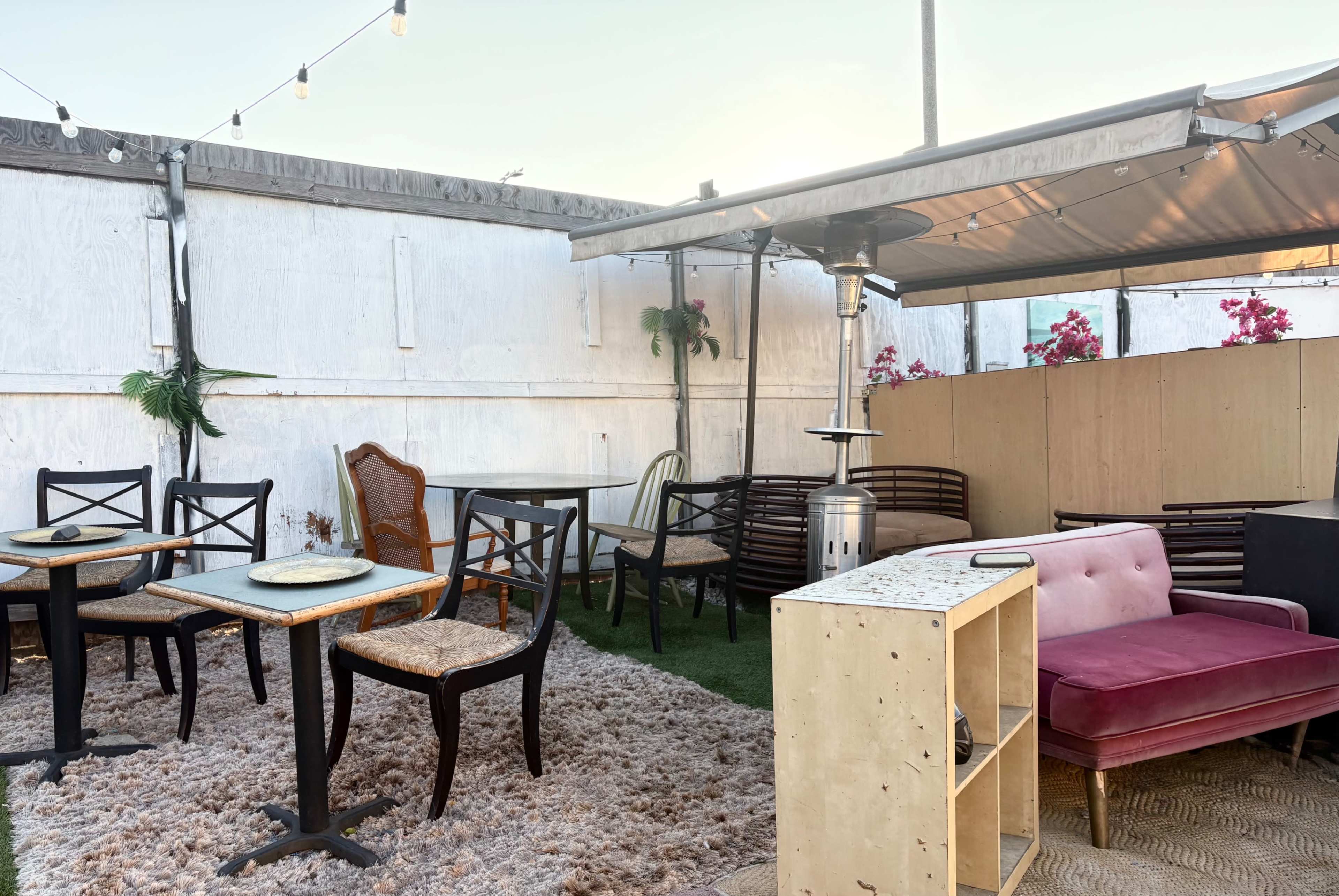 The image shows an outdoor seating area with various chairs and tables on a carpeted surface, along with a portable heater and decorative plants.