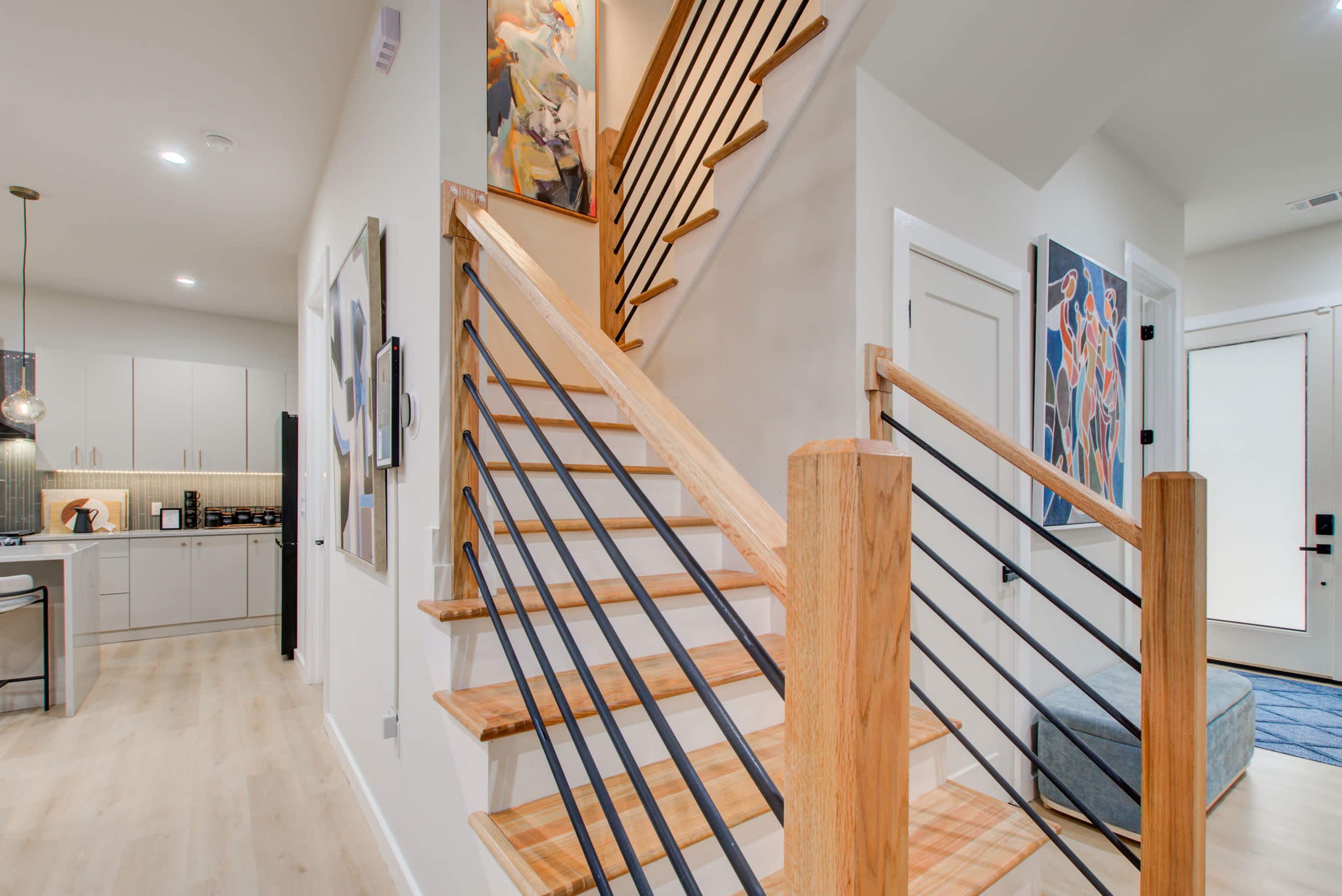 A modern interior hallway with a wooden staircase leading to an upper level, flanked by decorative artwork on the walls.