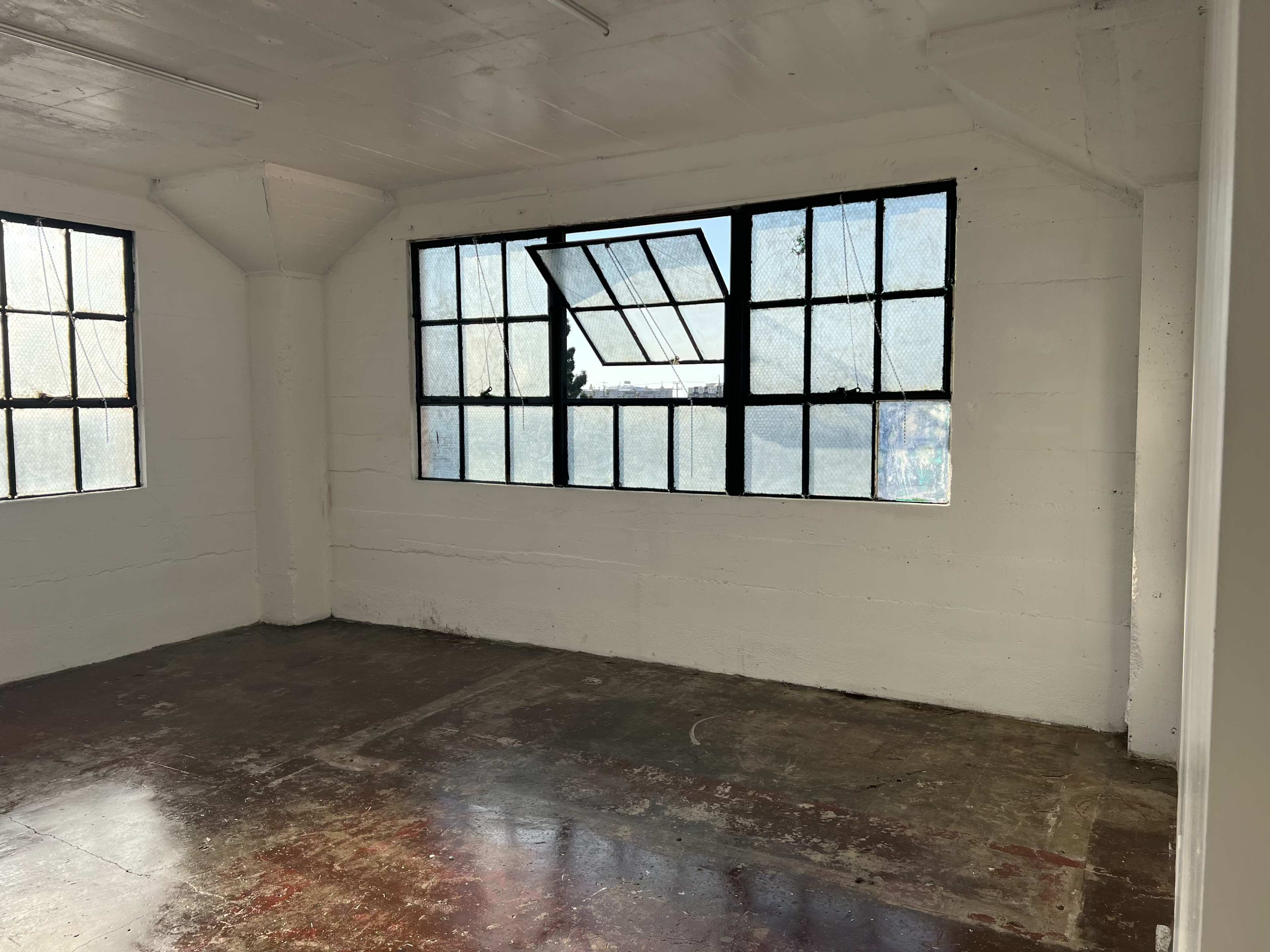 An empty room with large windows featuring metal frames and a concrete floor.