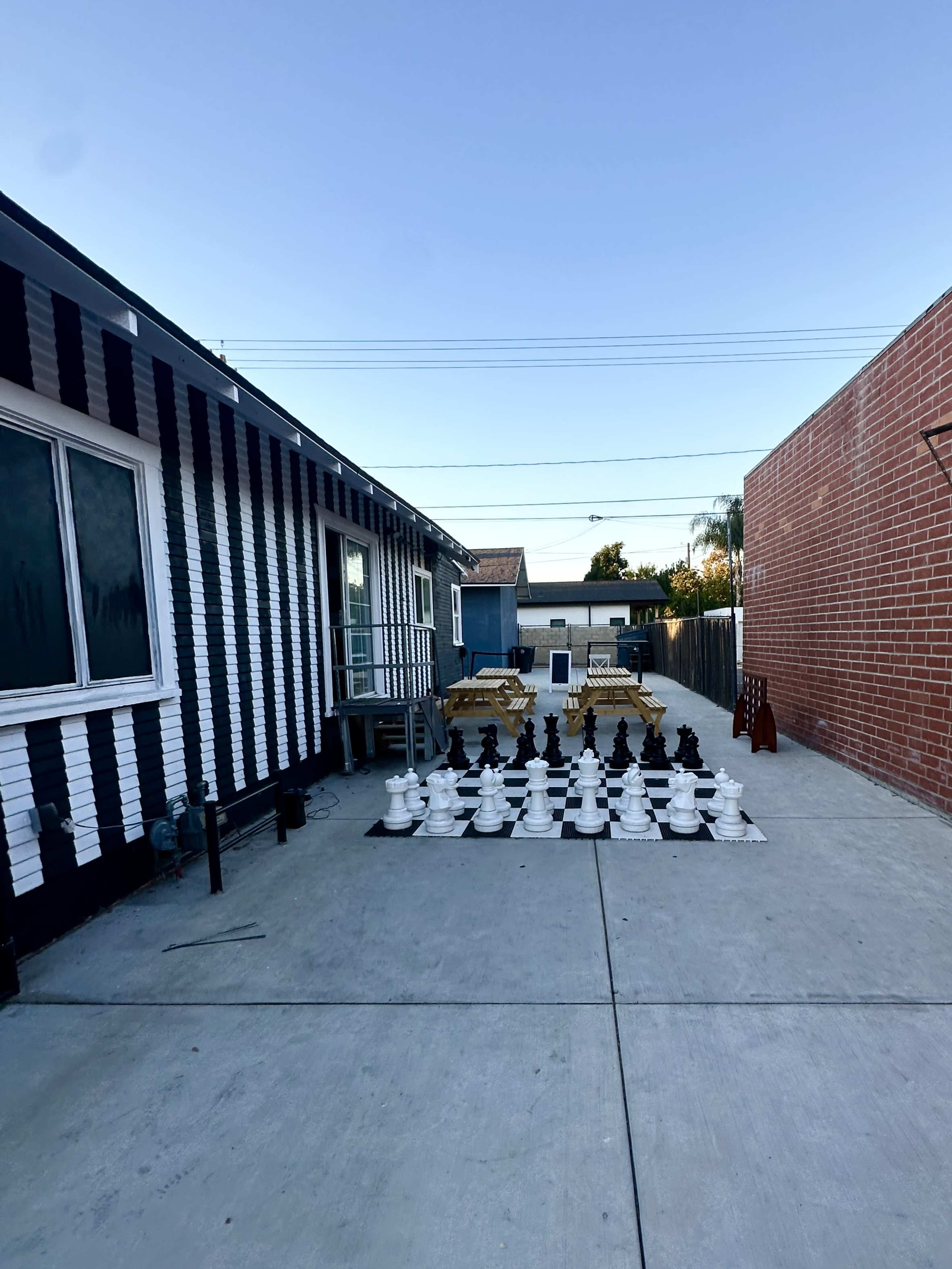 A large outdoor space features a striped building, a chessboard with oversized pieces, and seating areas in the background.