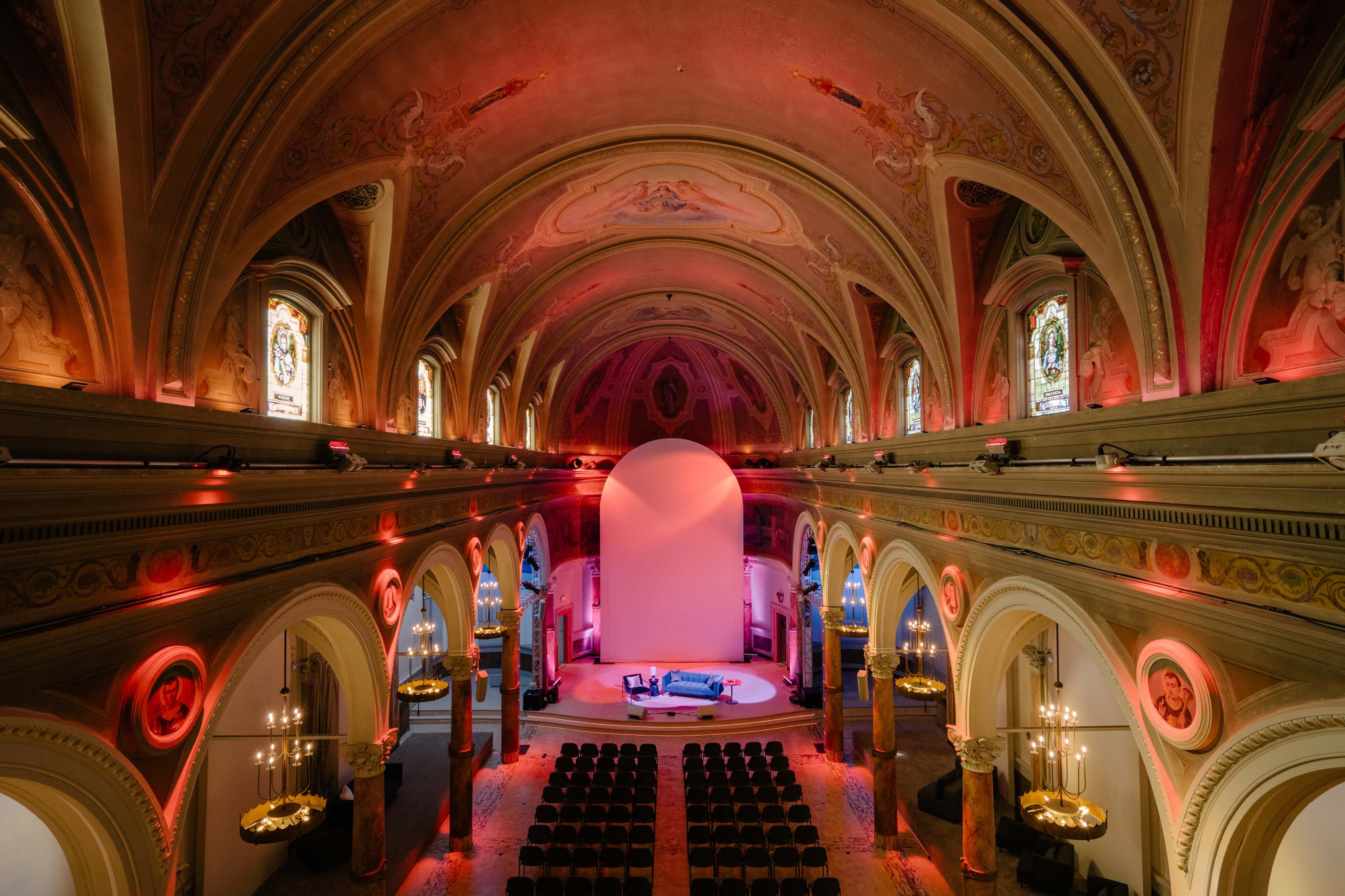 The interior of a grand church with an elevated view, featuring ornate architecture, stained glass windows, and a stage set for a performance.