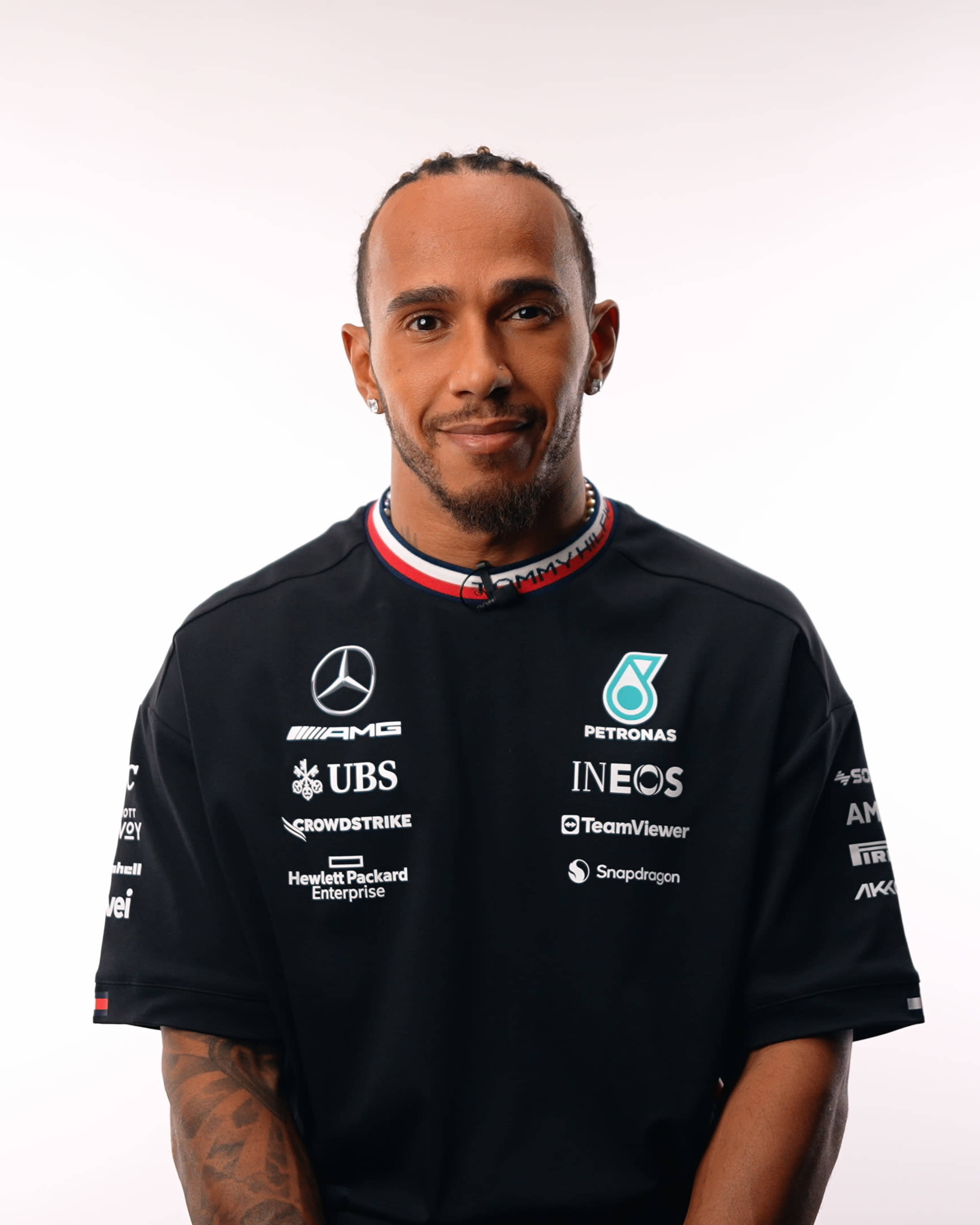 A man wearing a black sports jersey with logos stands against a plain background.