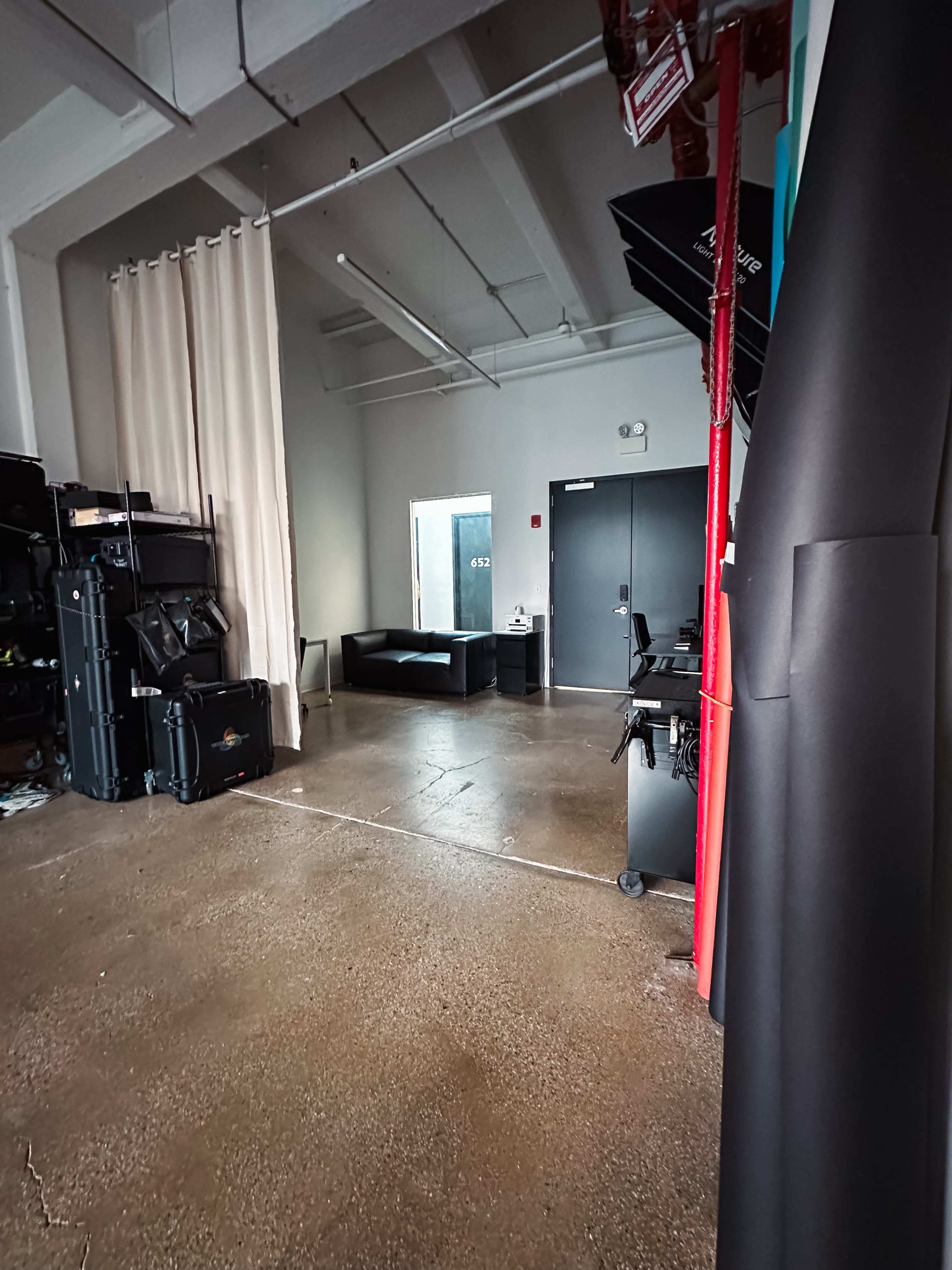 A spacious room with a concrete floor, a black sofa, a mirror, and various studio equipment lined against the walls.
