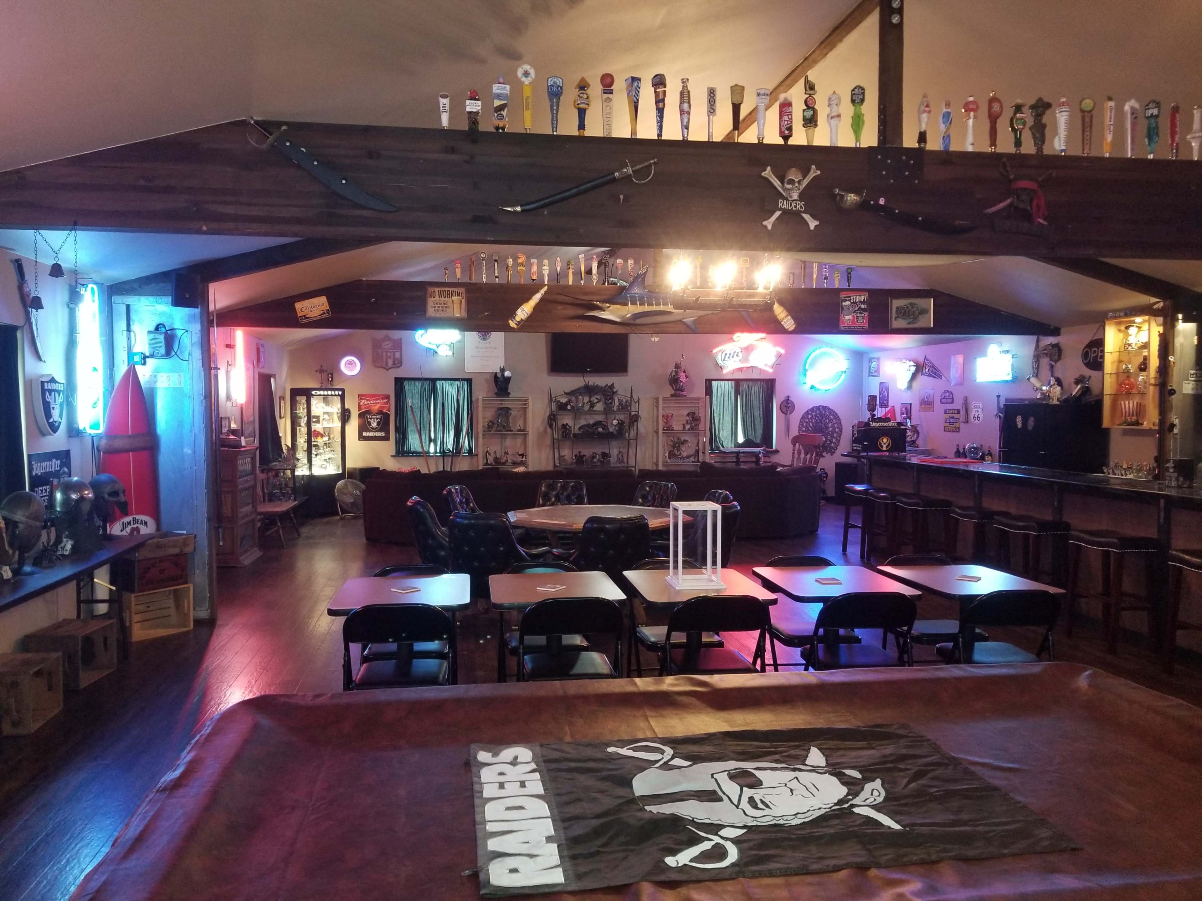 A recreational room with a bar area, seating arrangements, and various decorations, including neon signs and wall-mounted memorabilia.