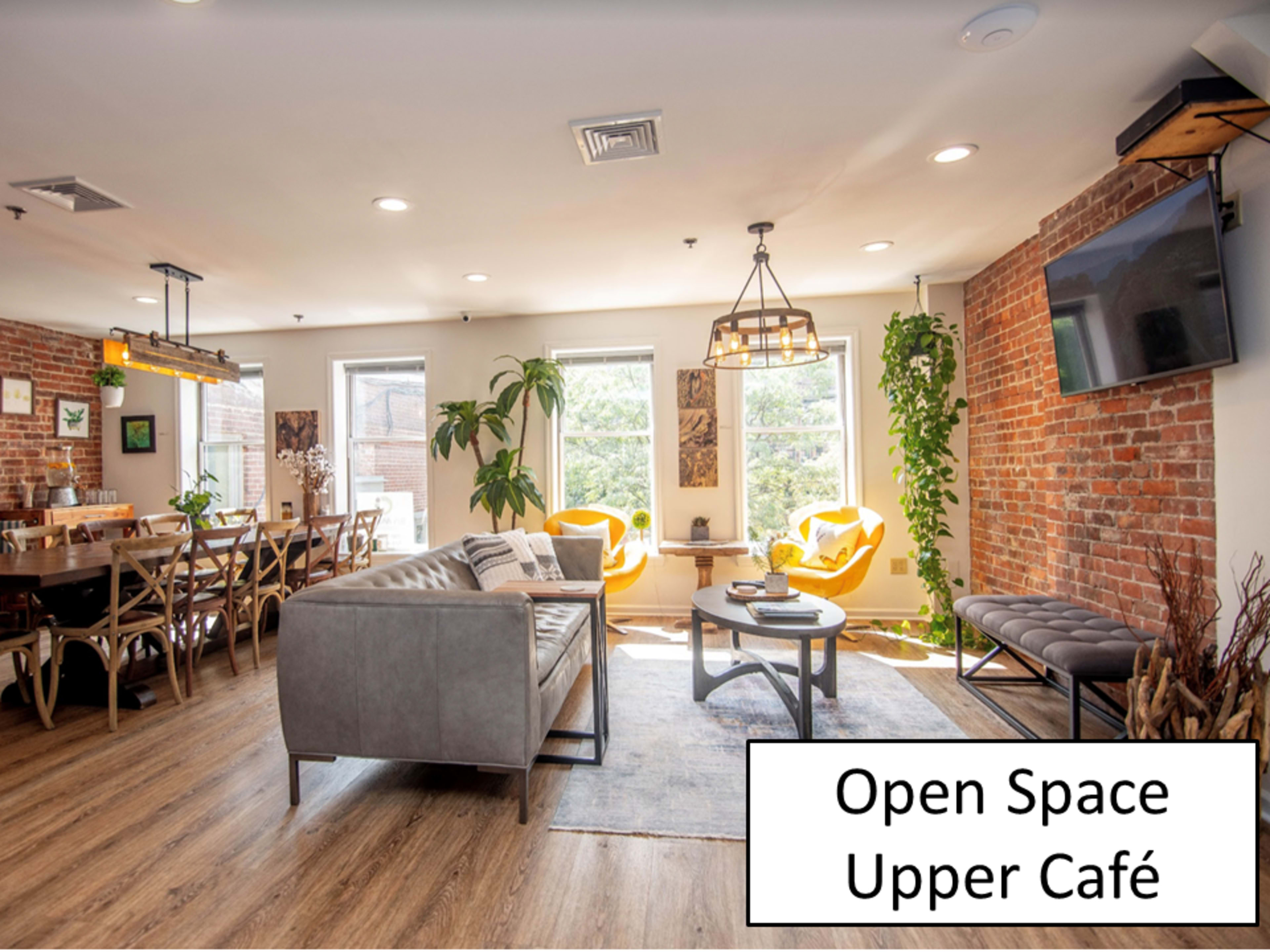 A brightly lit café with brick walls, modern furniture, and large windows overlooking greenery.