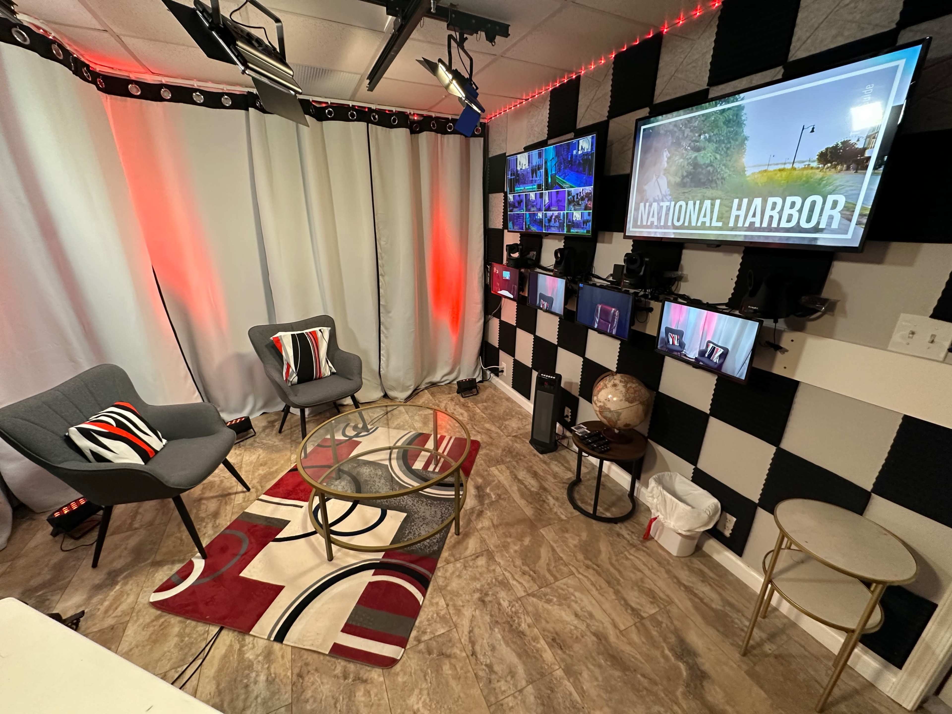 A modern studio setup with two chairs, a glass table, multiple screens displaying content, and a decorative rug.