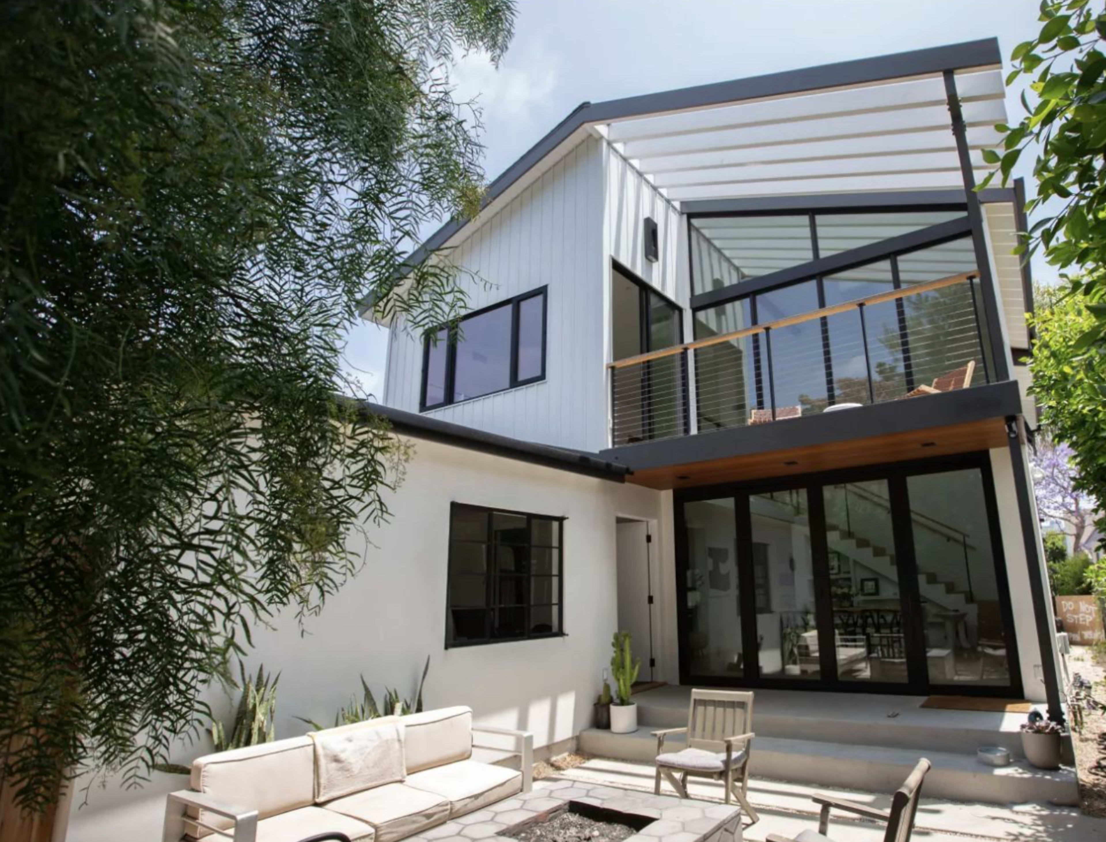 A modern two-story house with a combination of white and dark exterior elements, featuring large windows and a balcony.