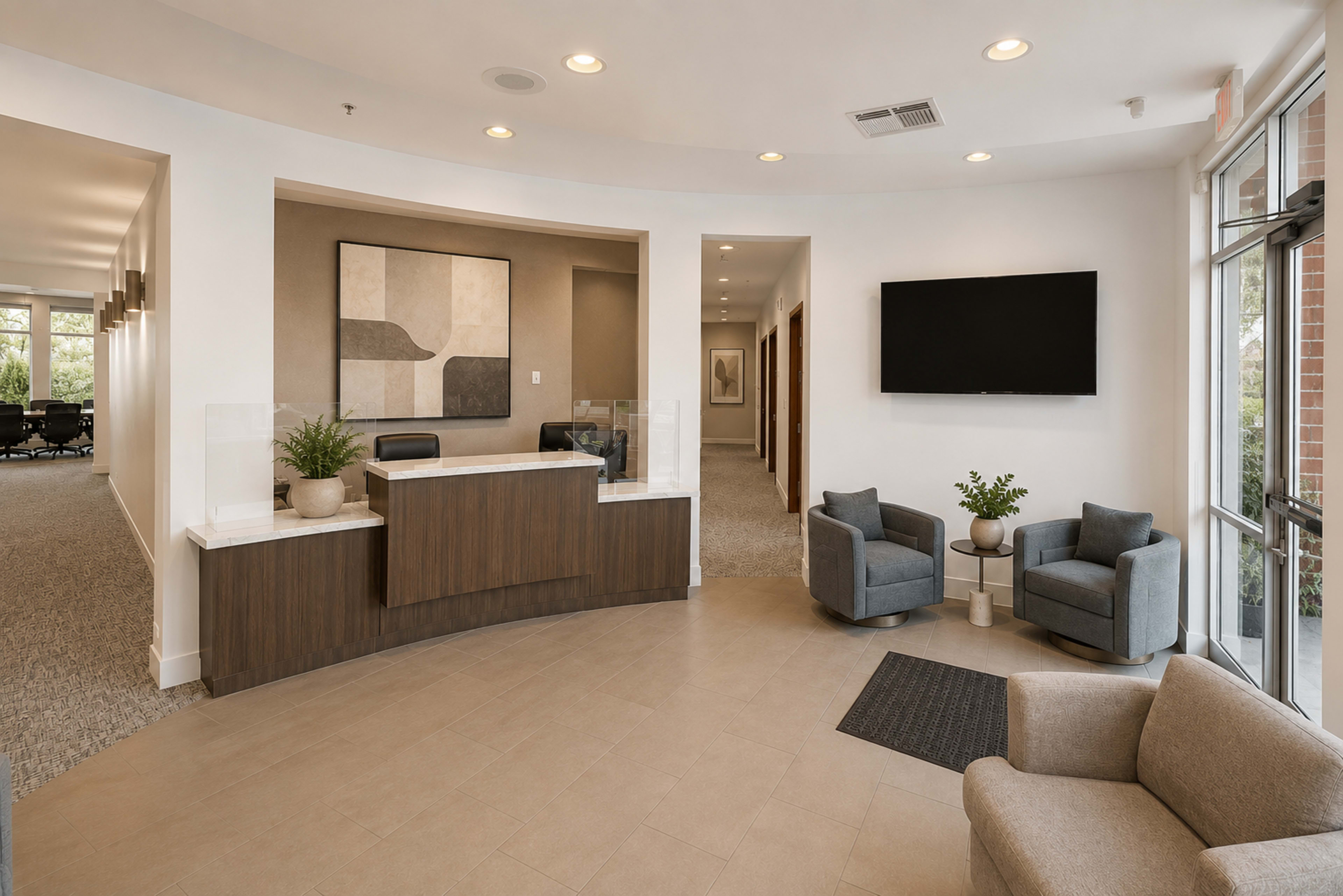 A modern reception area features a front desk, two seating areas with gray chairs, and a wall-mounted television.
