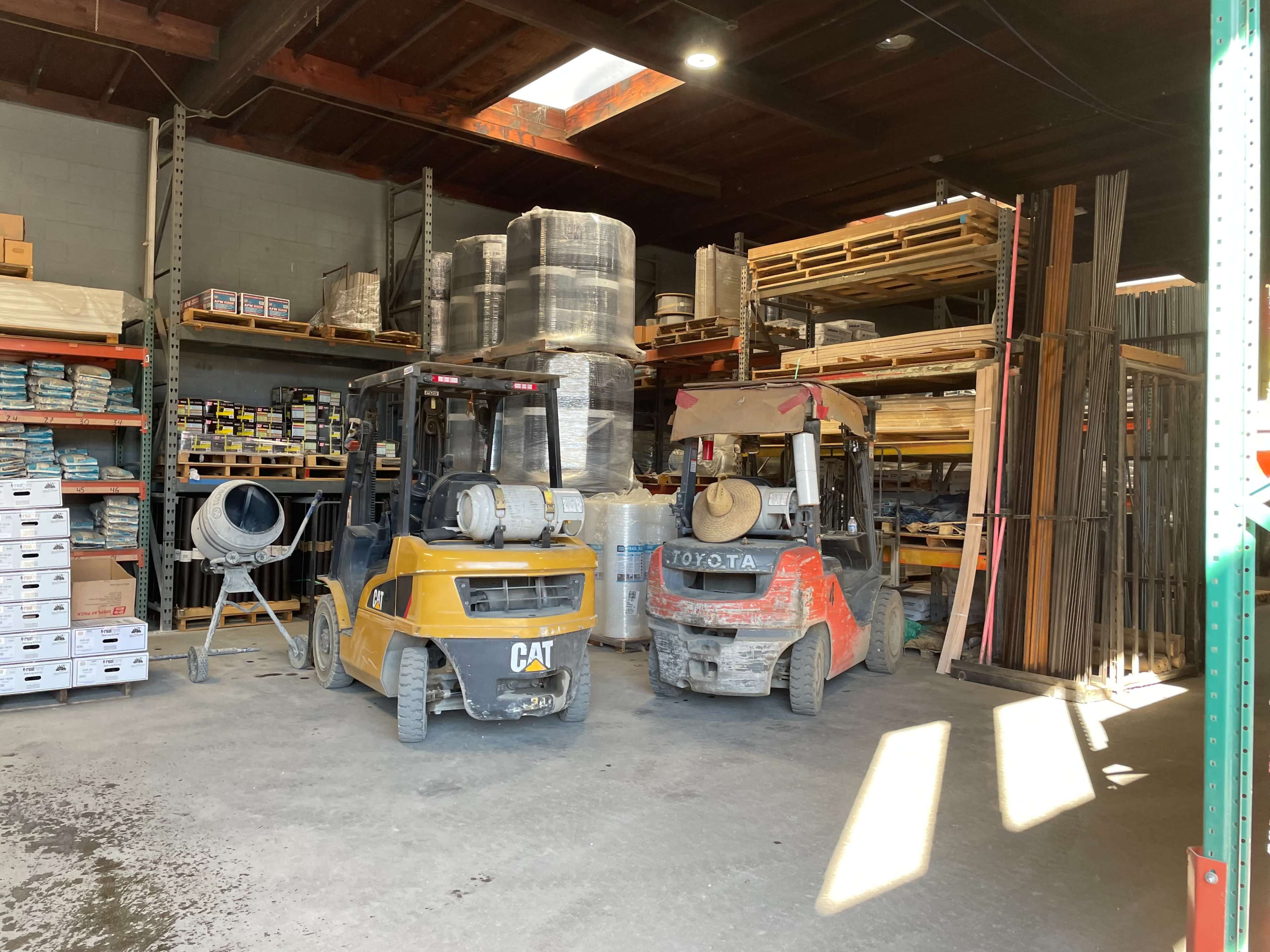 The image shows two forklifts parked in a warehouse surrounded by stacks of building materials and supplies.