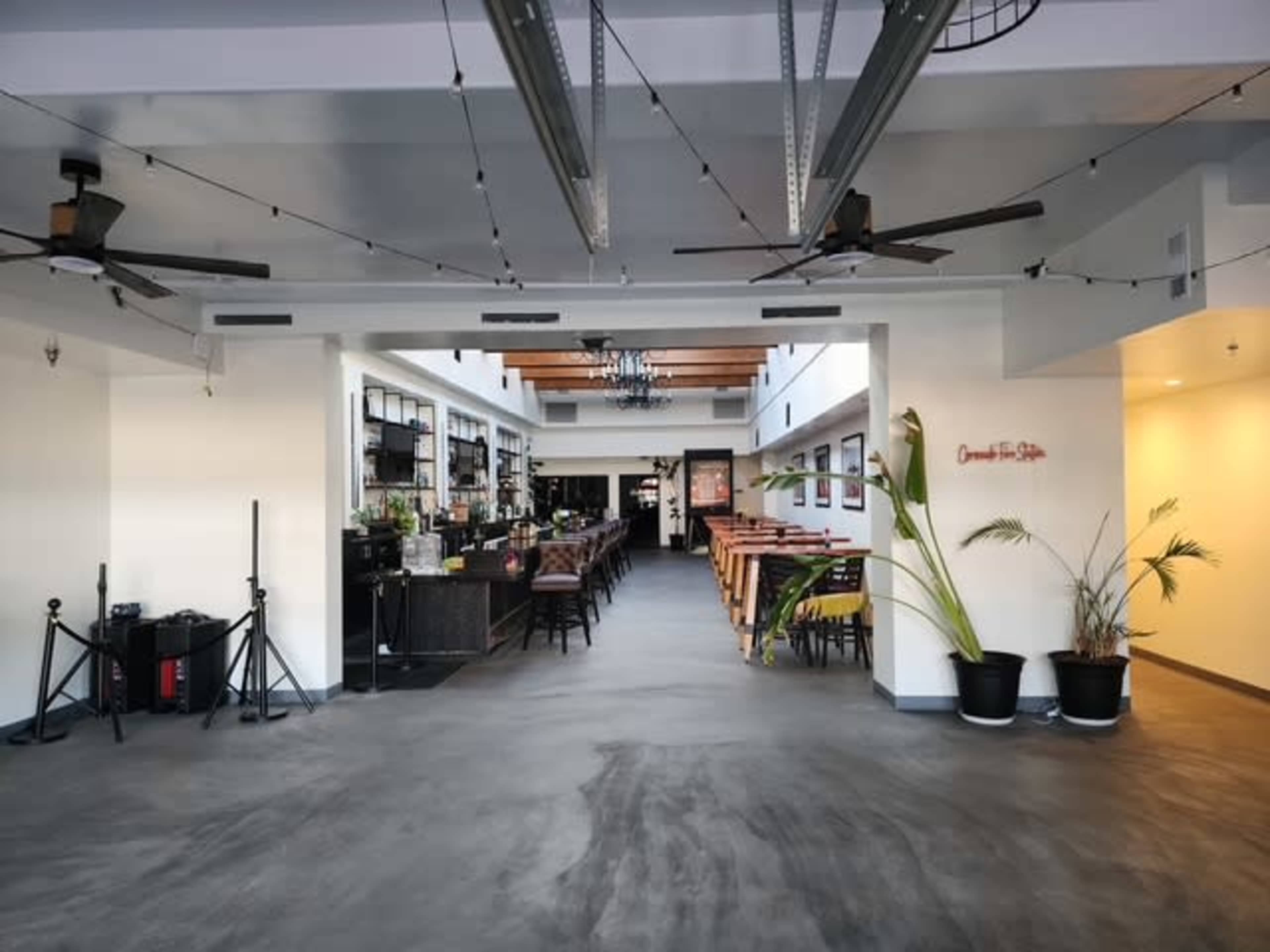 The image shows an indoor dining area of a restaurant with a straight corridor, wooden tables and chairs, and wall shelves displaying glassware.