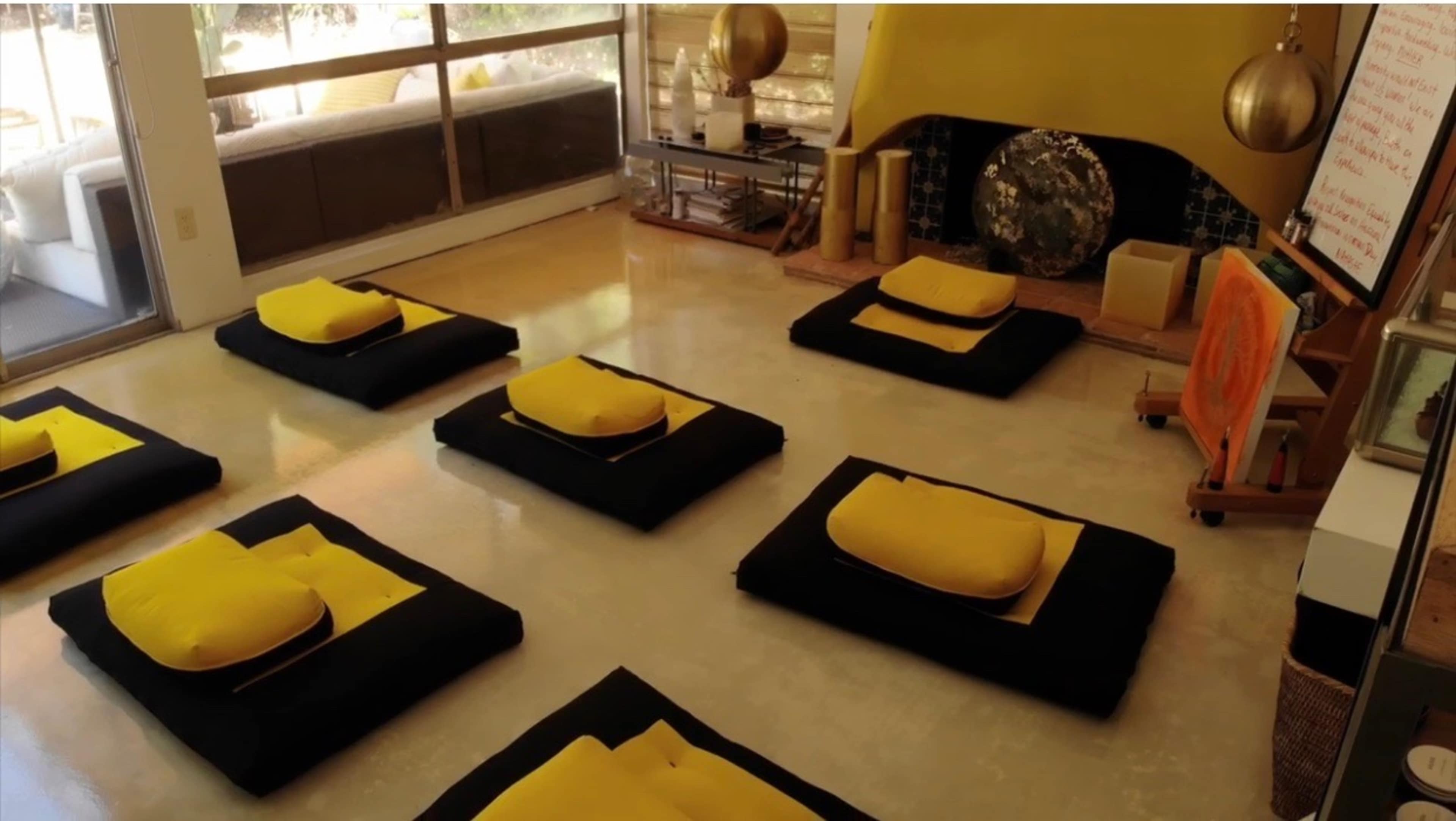 A spacious room with several black cushions topped with yellow pillows arranged on a smooth floor, surrounding a decorative fireplace.