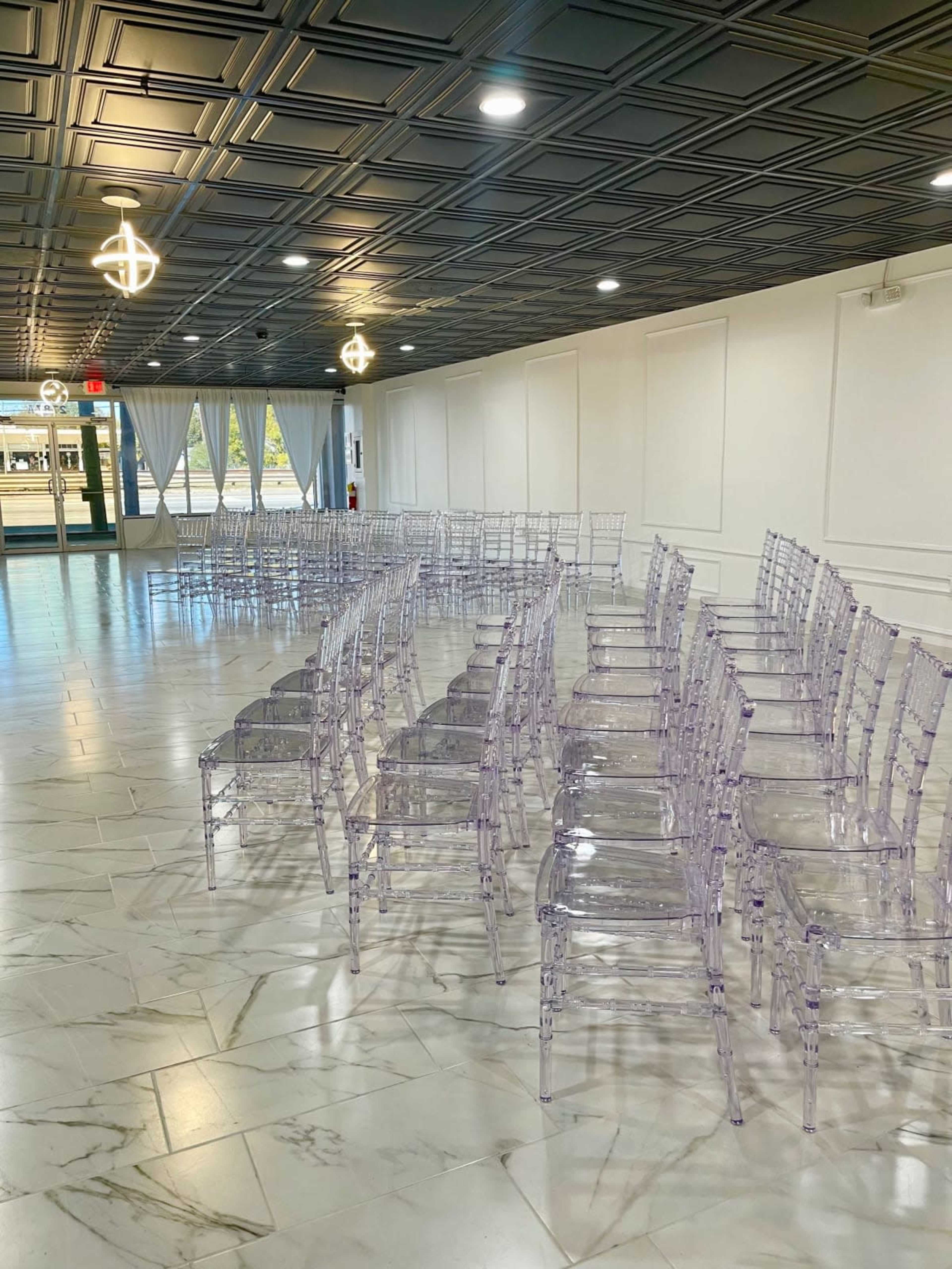 A row of transparent chairs is arranged in a neat formation on a marble floor in a well-lit indoor space.