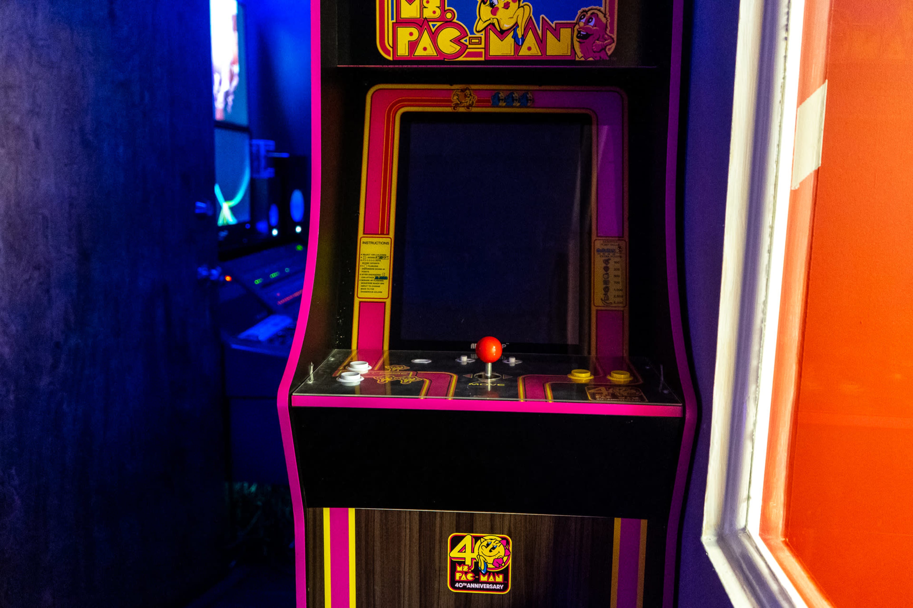 A vintage Ms. Pac-Man arcade machine stands against a wall in a dimly lit gaming area.