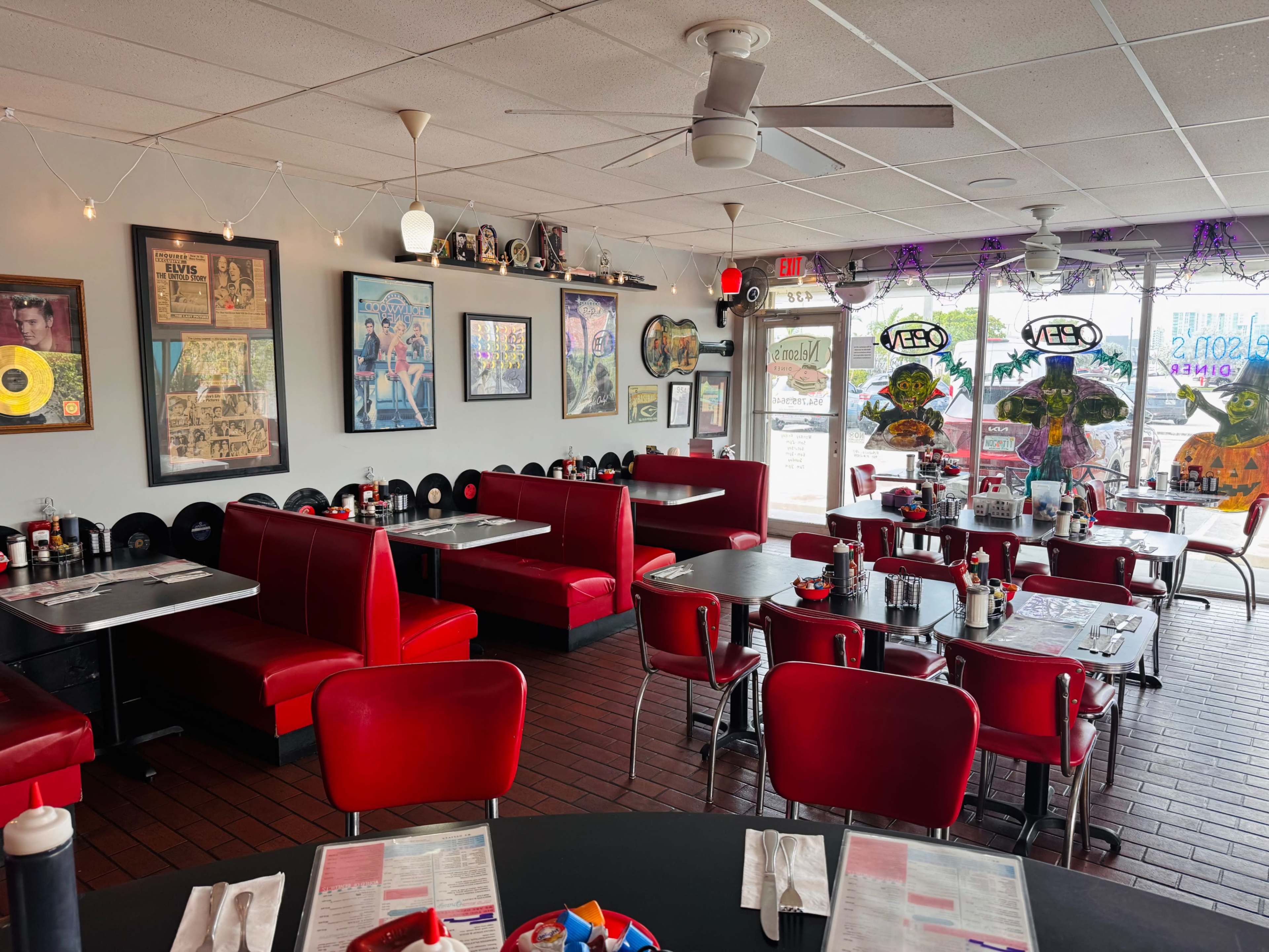 The image shows a diner interior with red booths, black tables, and wall decorations featuring vintage records and framed photos.