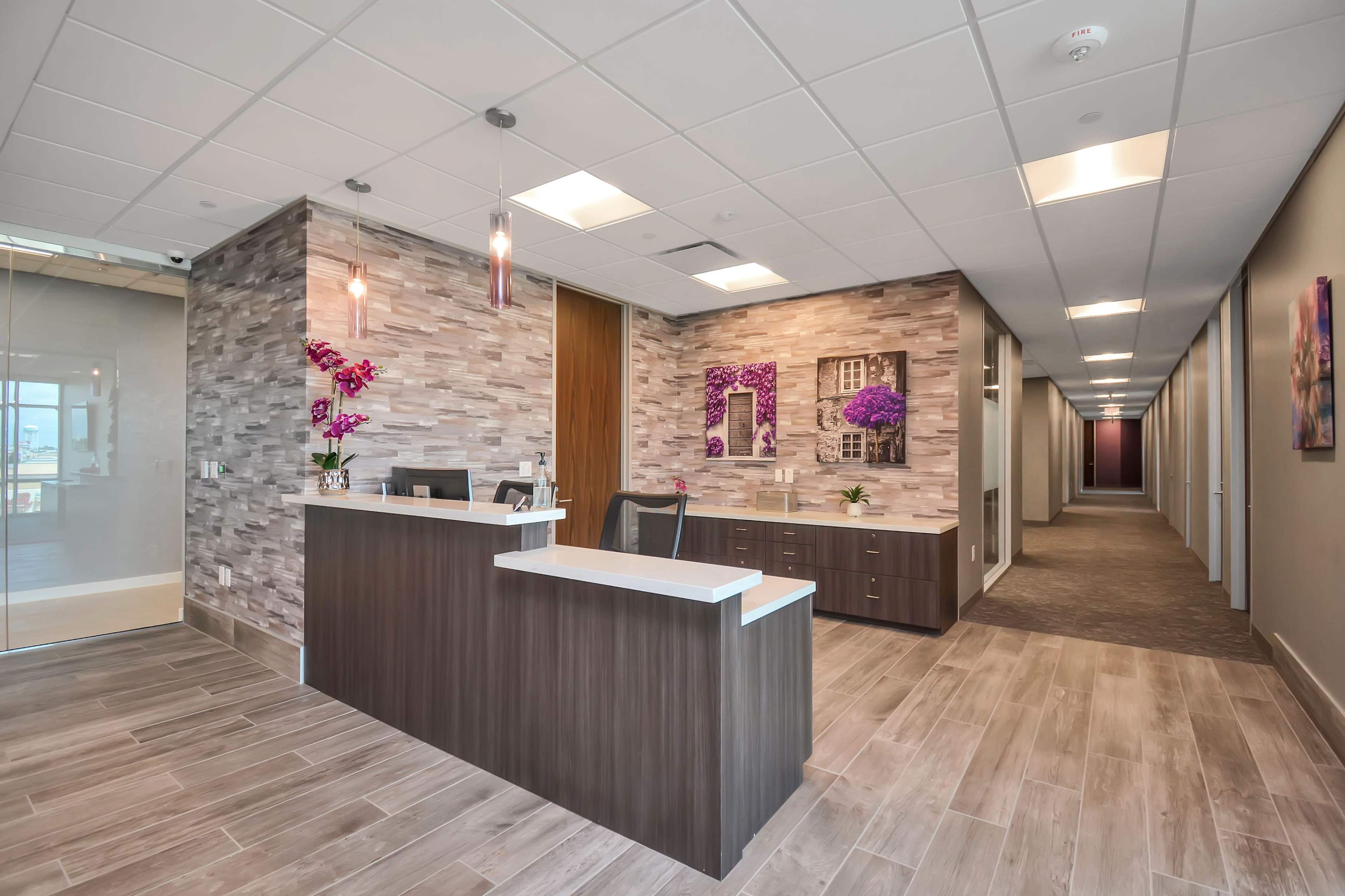 A modern reception area with a front desk, decorative wall art, and a corridor leading to offices in the background.
