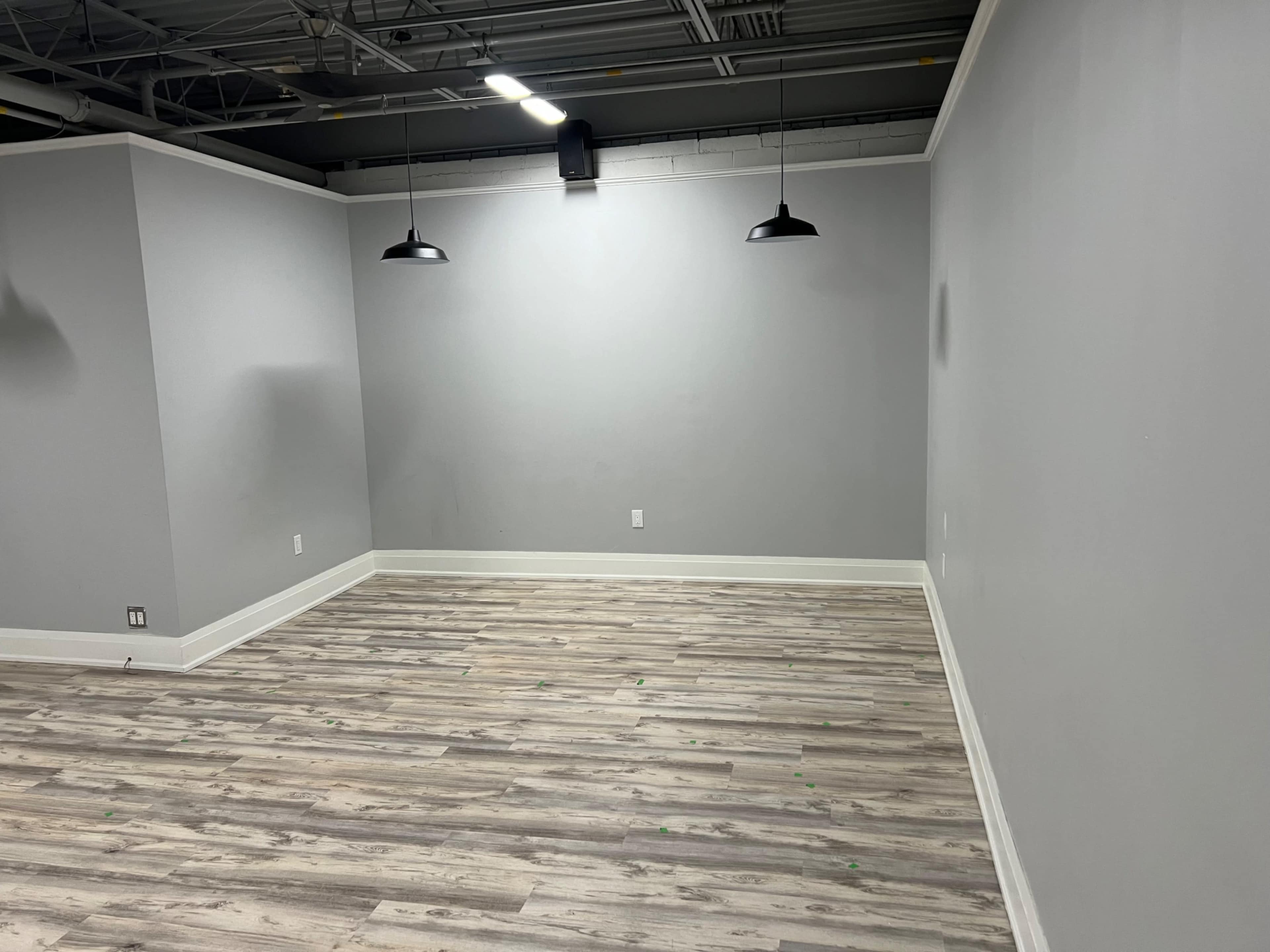 An empty room with gray walls and laminate flooring, featuring two black pendant lights hanging from the ceiling.