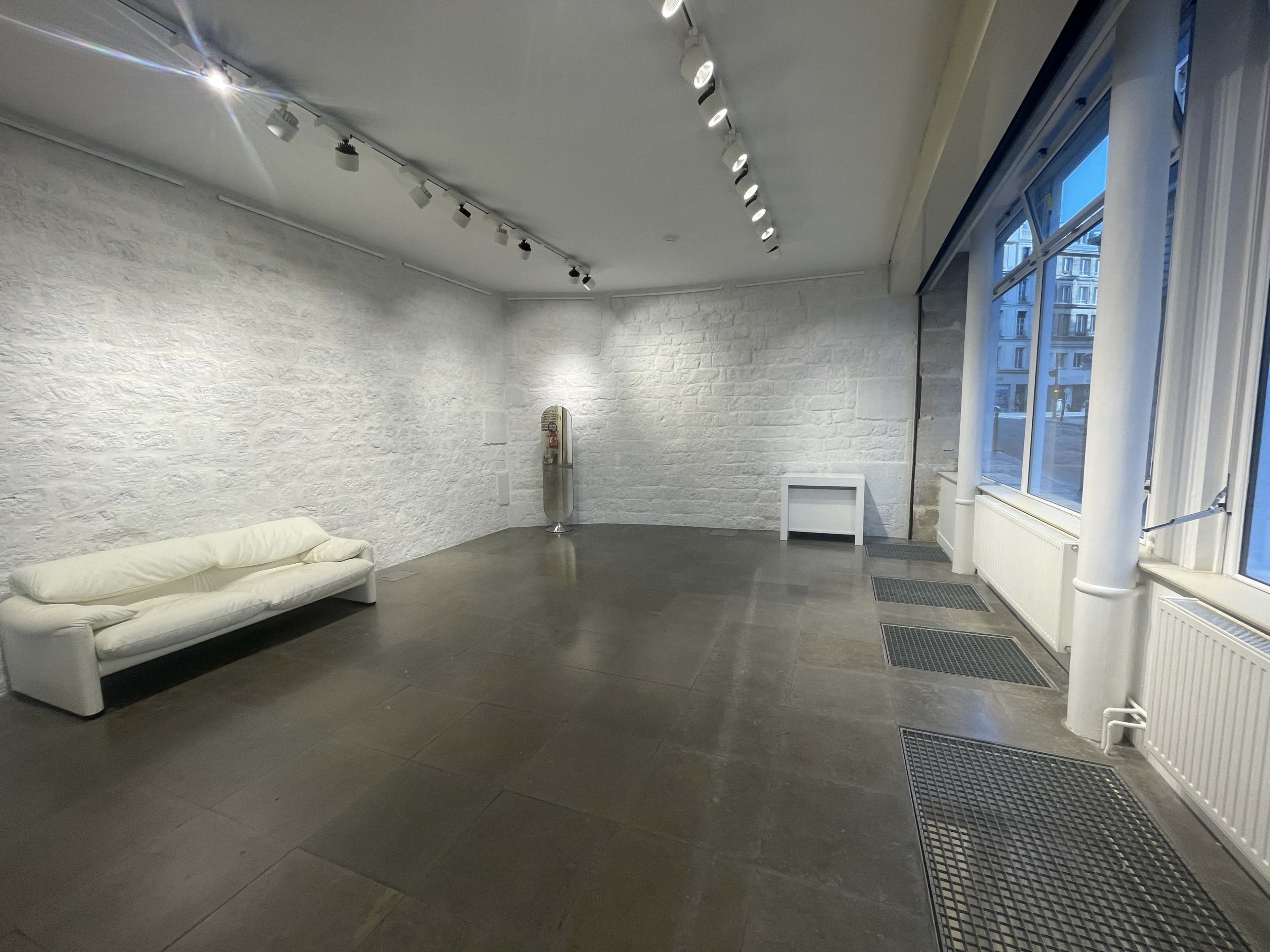 A spacious, empty room with a white couch, a side table, and large windows allowing natural light to enter.