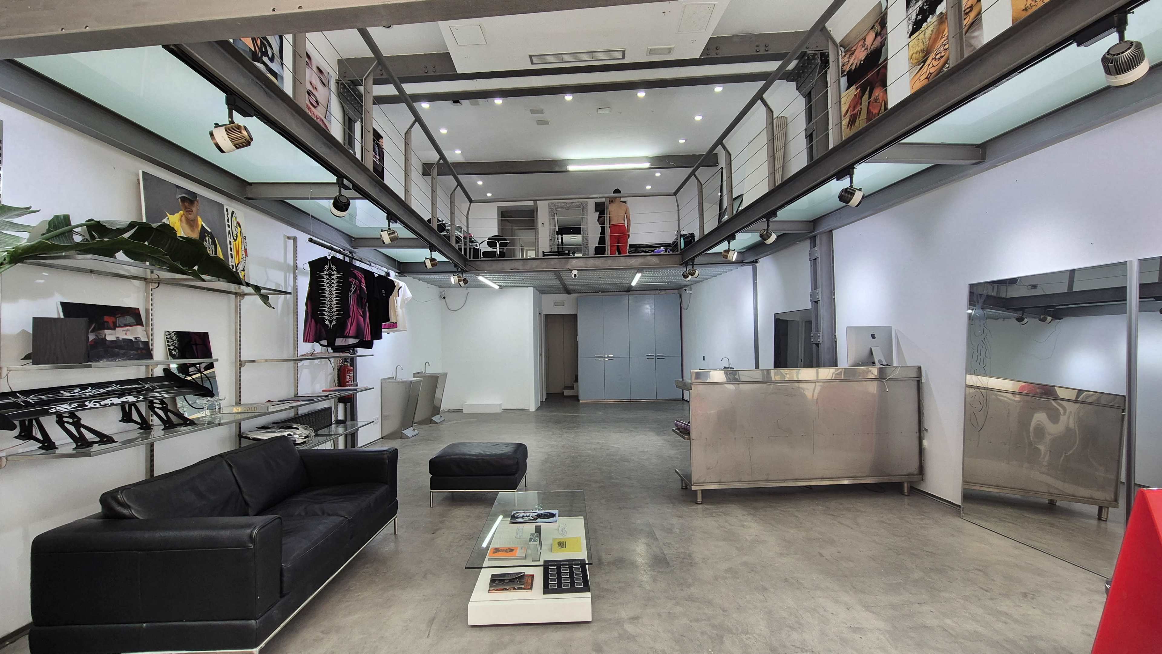 The image shows a modern retail space with minimalist design, featuring a black sofa, a glass coffee table, and a shiny metal reception area.