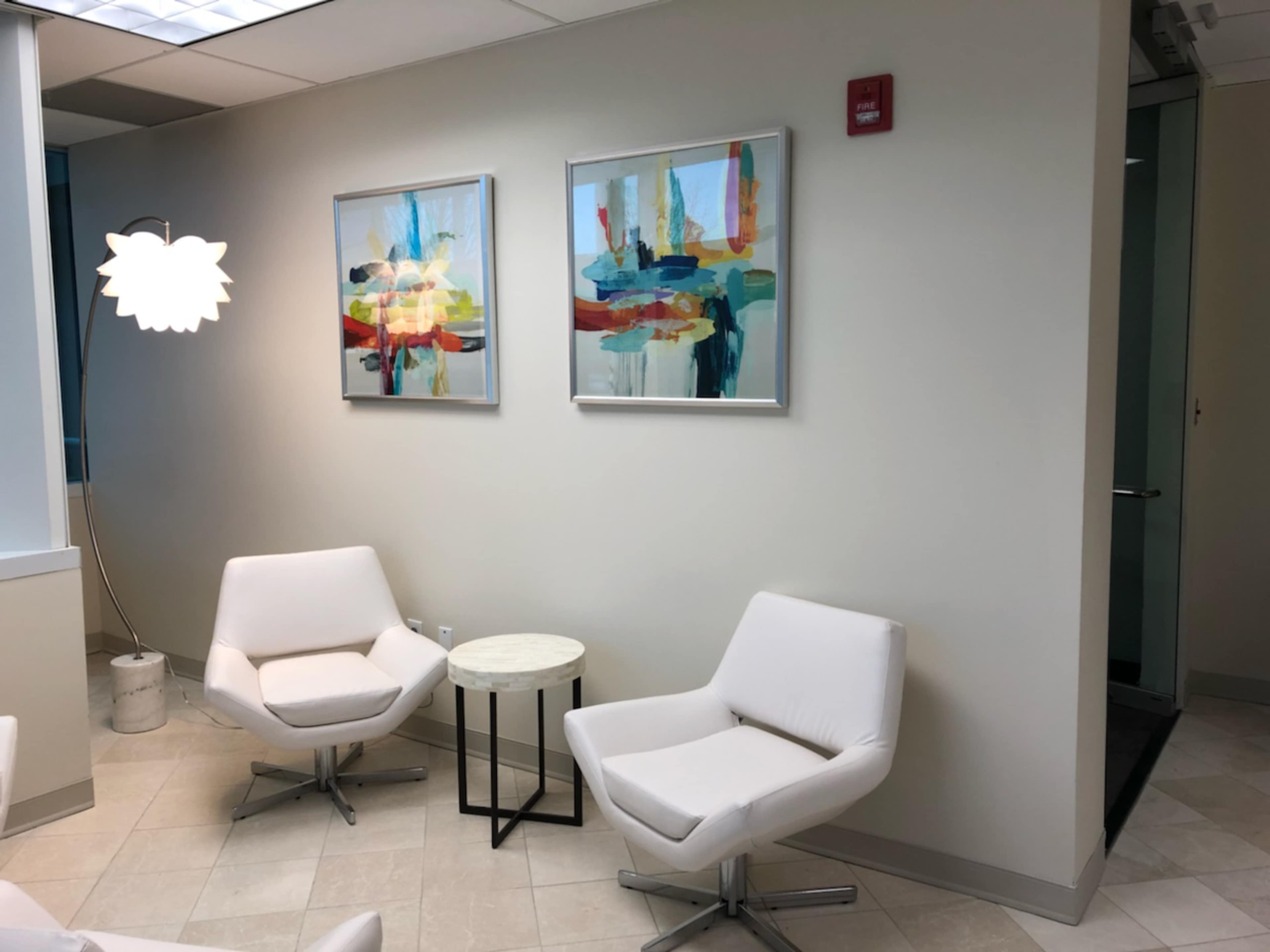 A modern waiting area with two white chairs, a small round table, and abstract artwork on the walls.